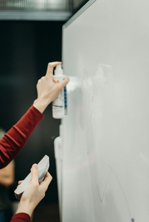 Person spraying whiteboard cleaner, holding eraser.