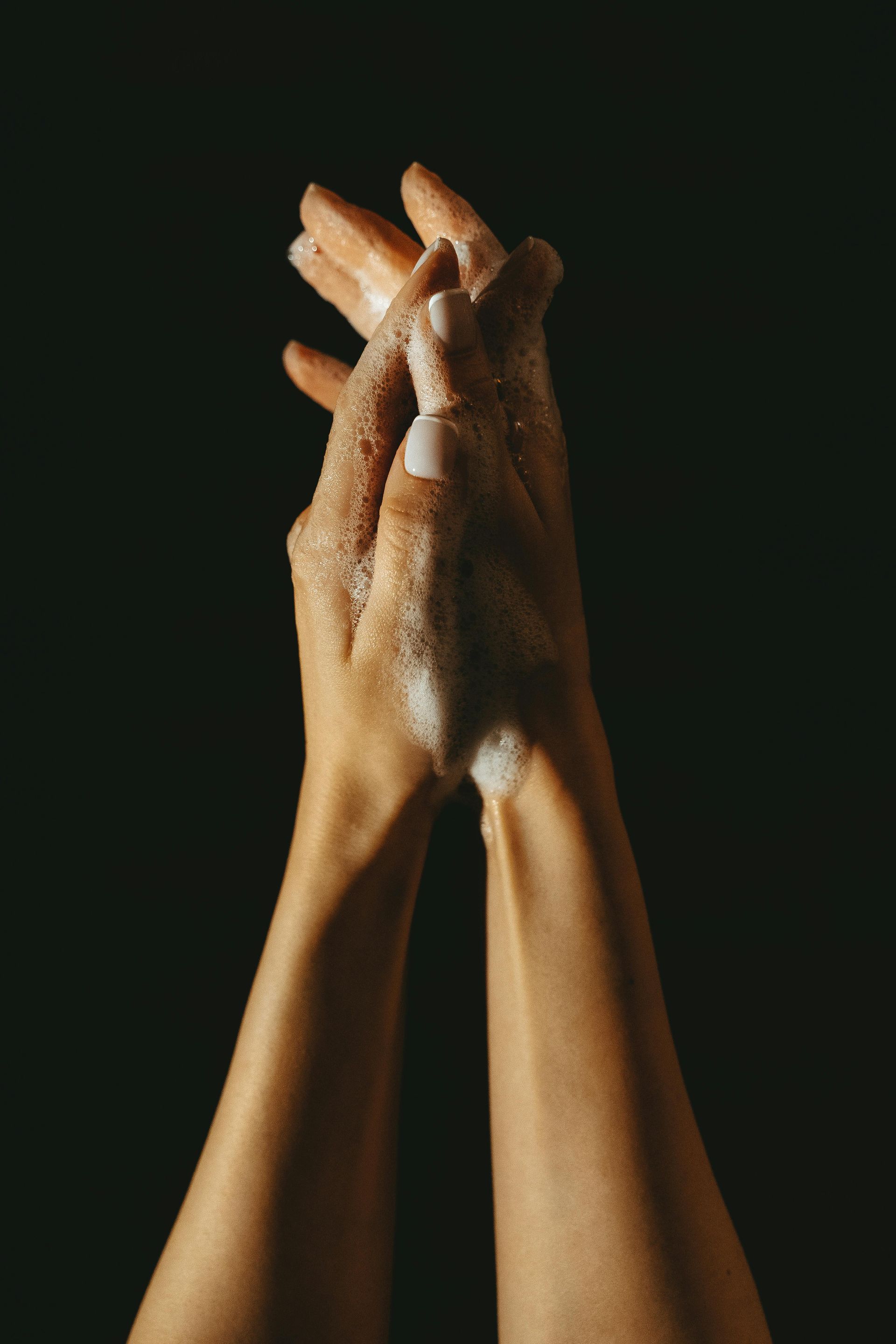 Hands clasped, lathered in soap, against a black background.