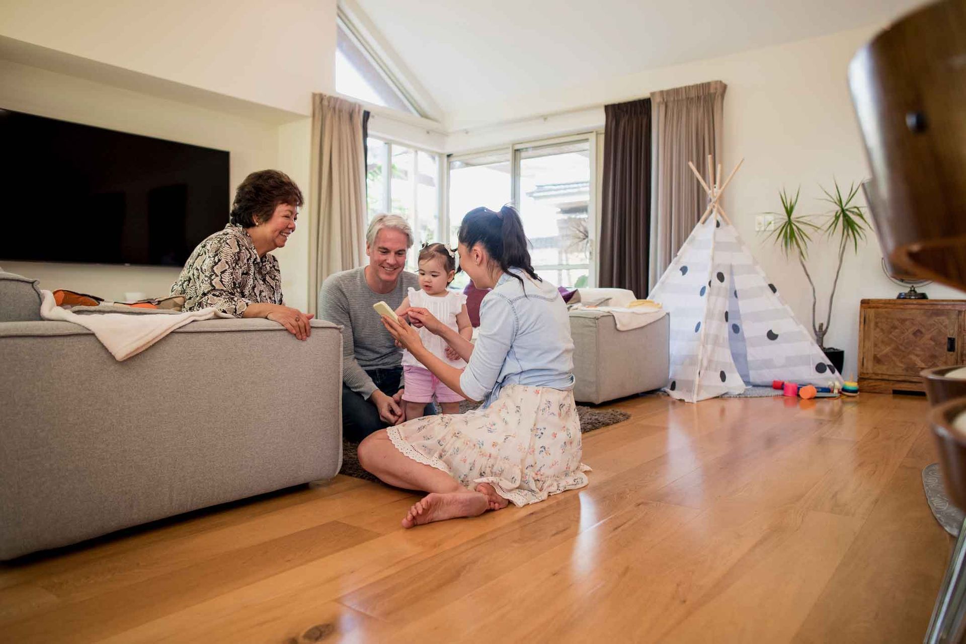 A family is sitting on the floor in a living room playing with a baby.
