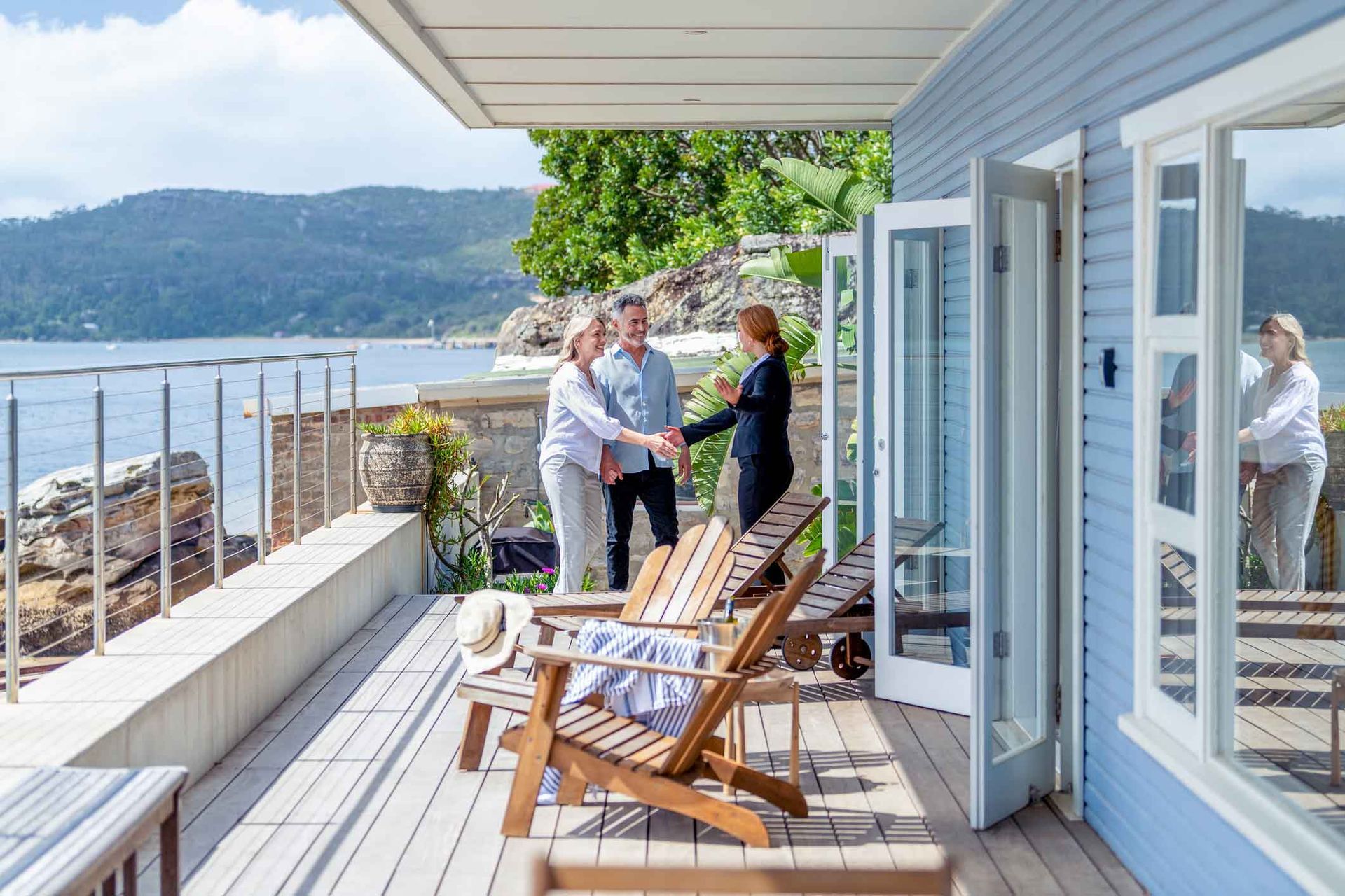 A man and woman are shaking hands on a deck overlooking a body of water.