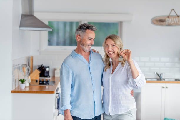 A man and a woman are standing in a kitchen holding keys to their new home.