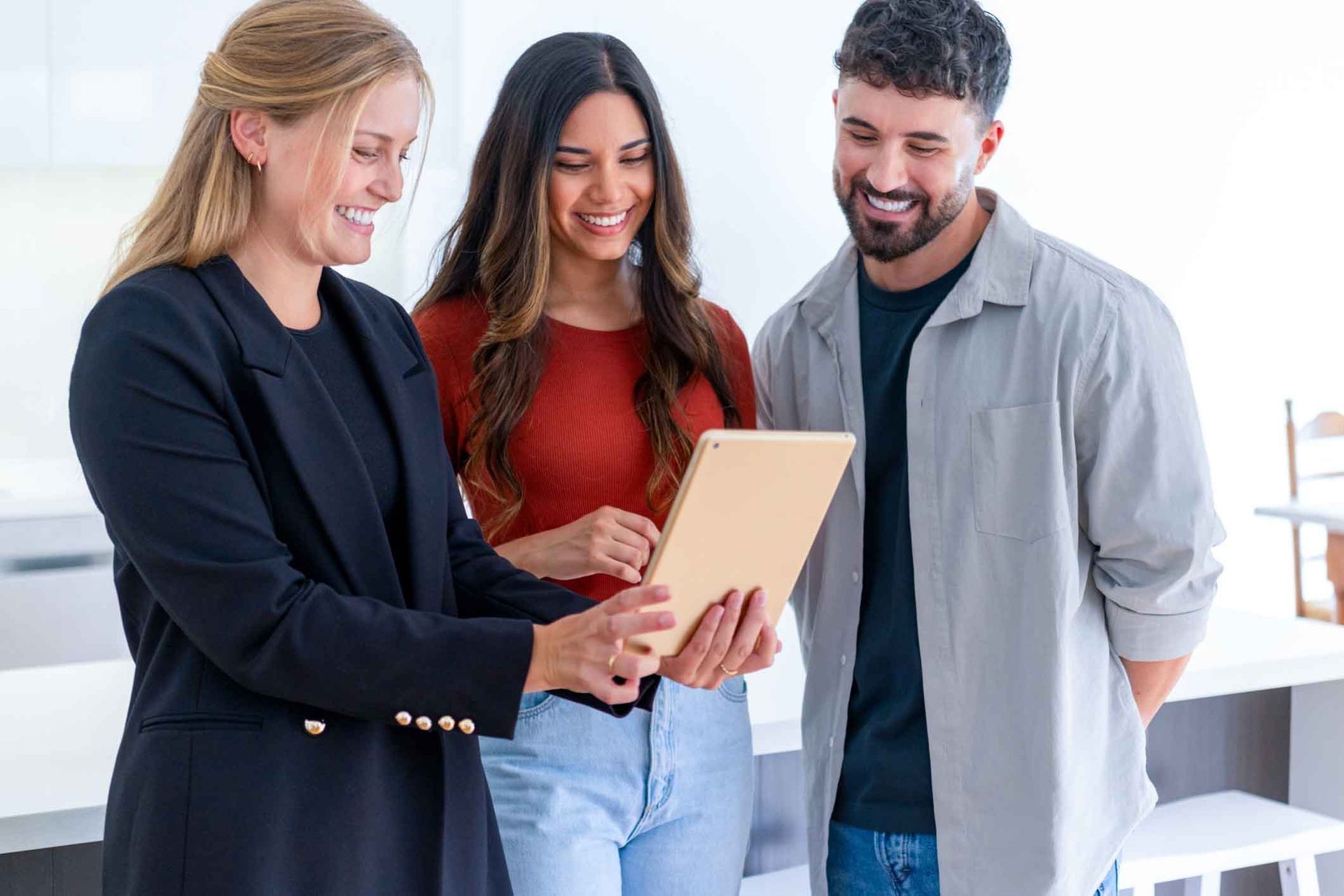 A woman is standing next to a man and a woman looking at a tablet.