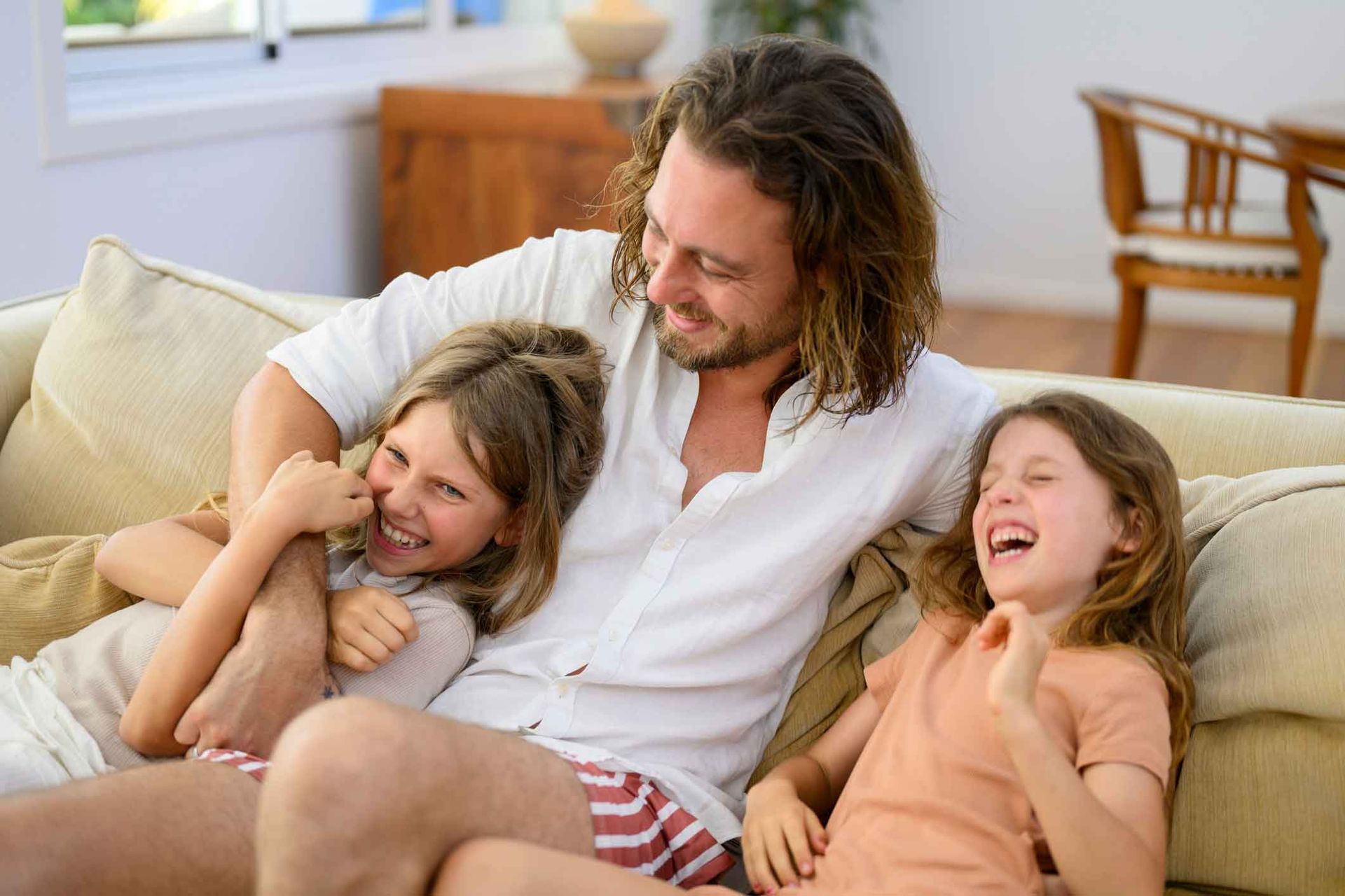 A man and two girls are sitting on a couch laughing.