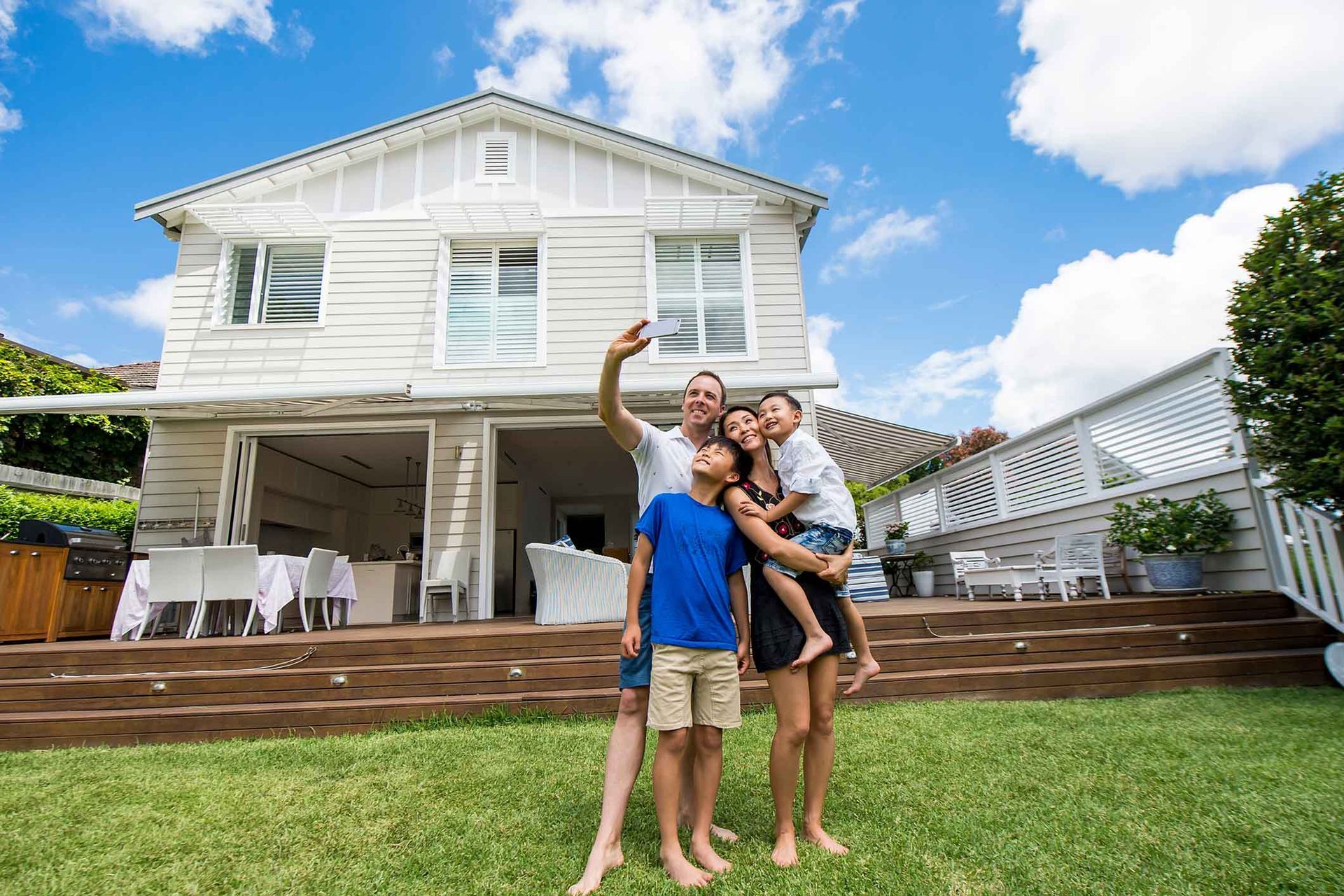 Family smiles and waves in a bright living room; parents, two young children.