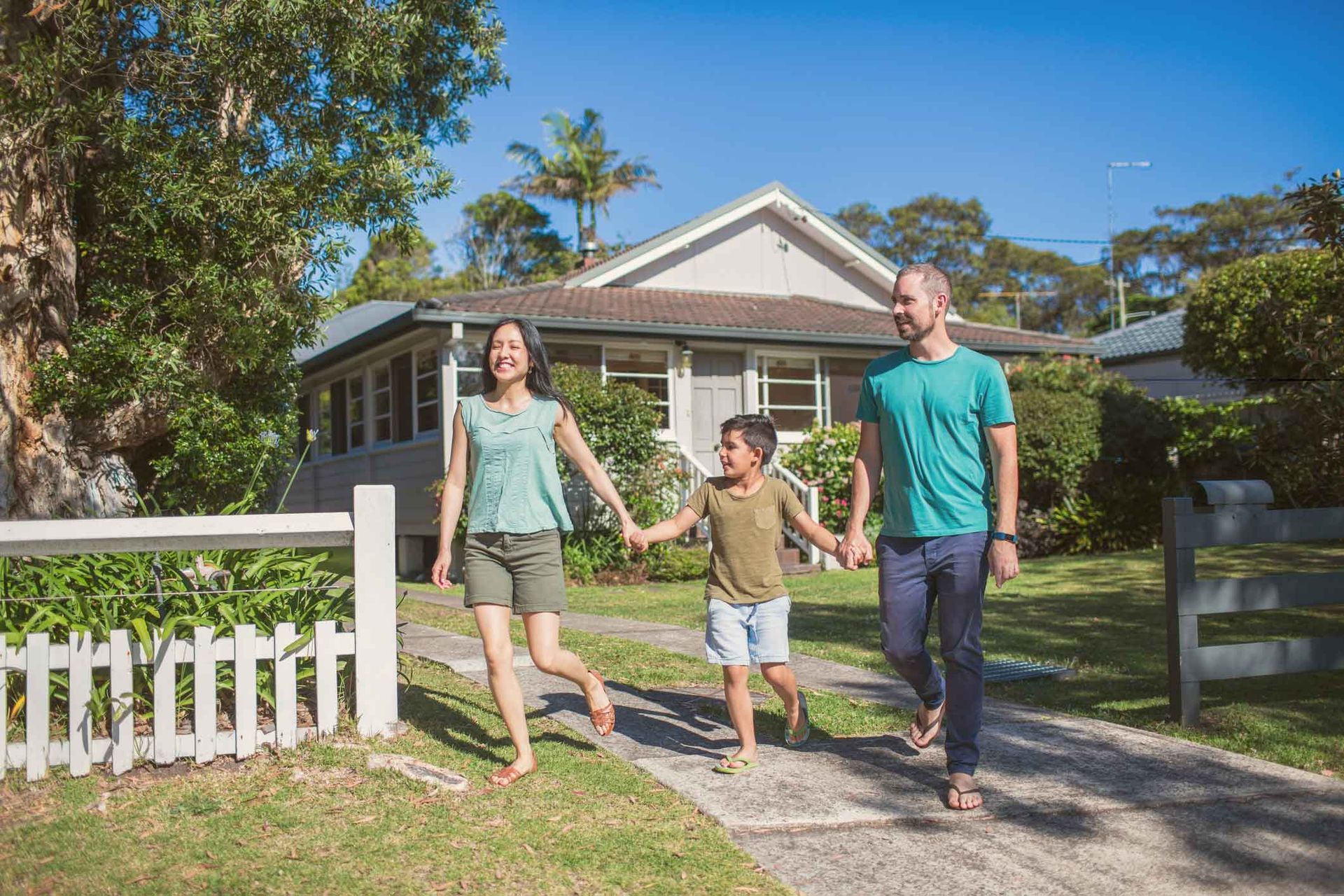 A family is walking down the sidewalk in front of their house holding hands.