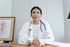 A female doctor is sitting at a desk with her hands folded.