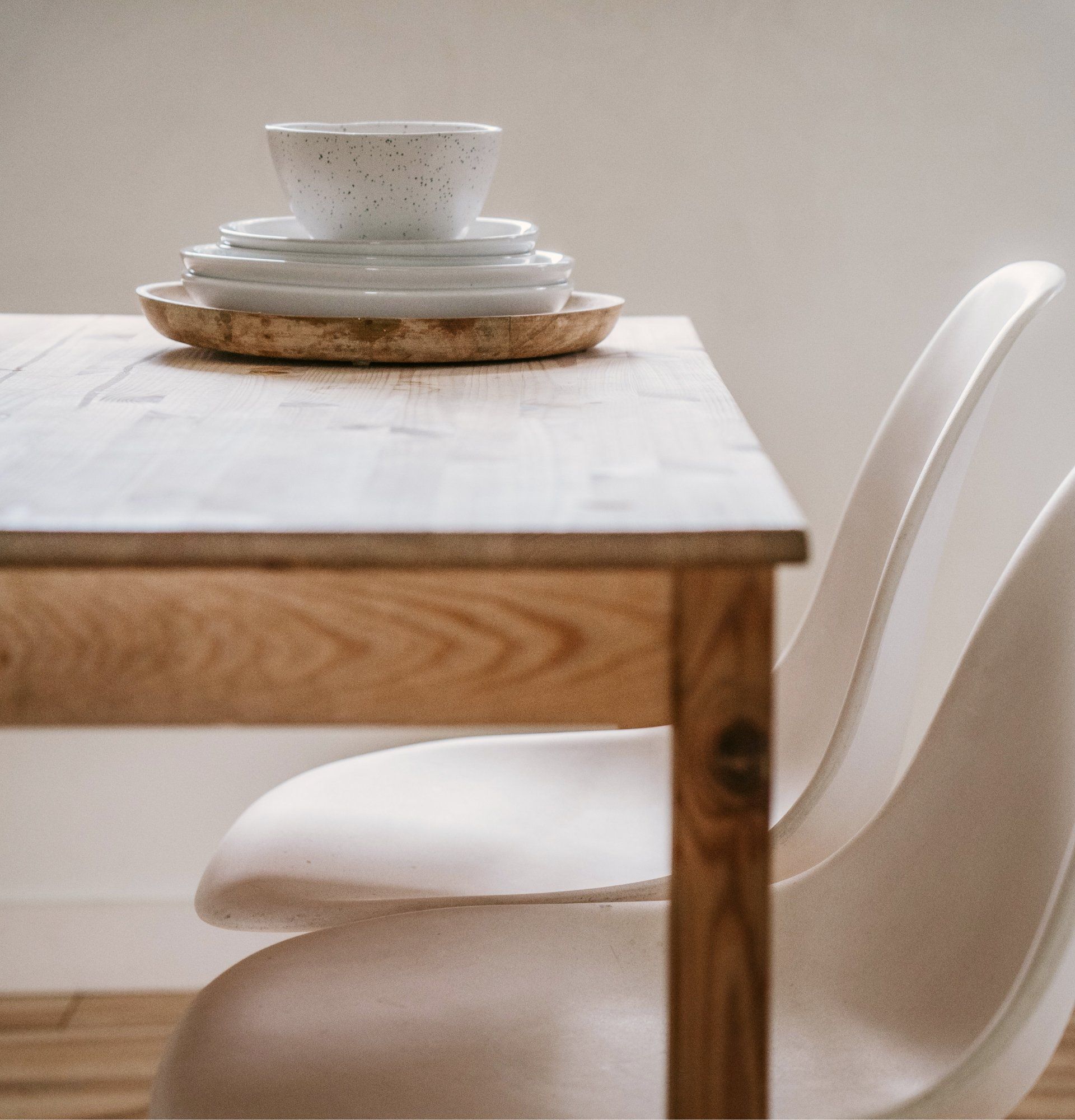Dining table set with white chairs and stacked dishes on a wooden tabletop