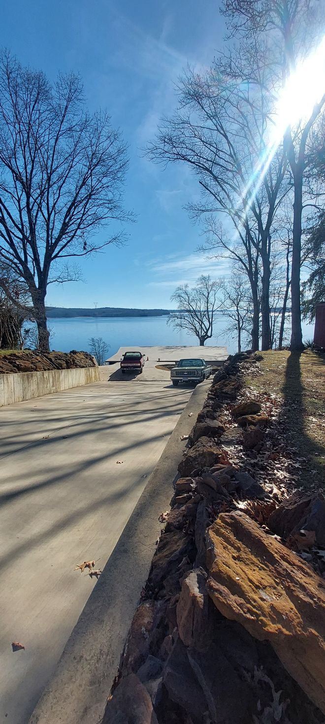 A car is driving down a road next to a lake on a sunny day.