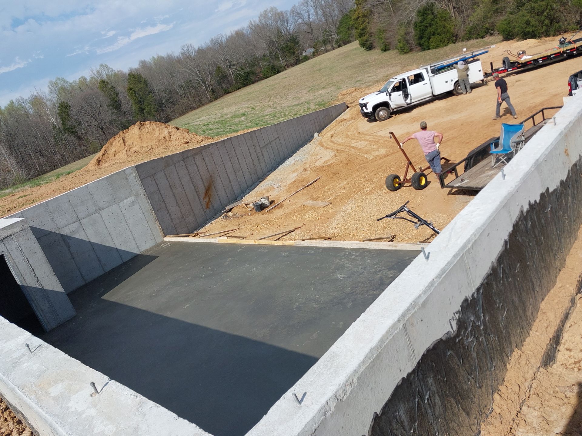 A man is pushing a wheelbarrow in front of a large concrete wall.