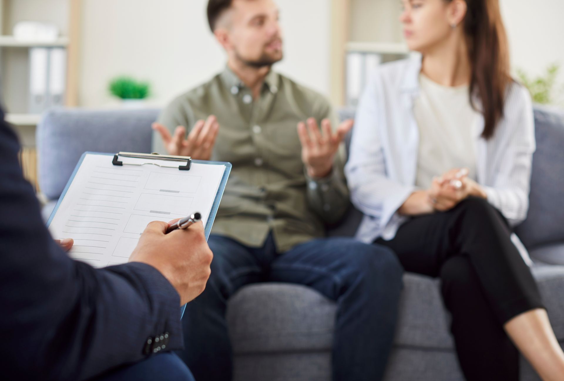A man and a woman are sitting on a couch talking to a counselor.