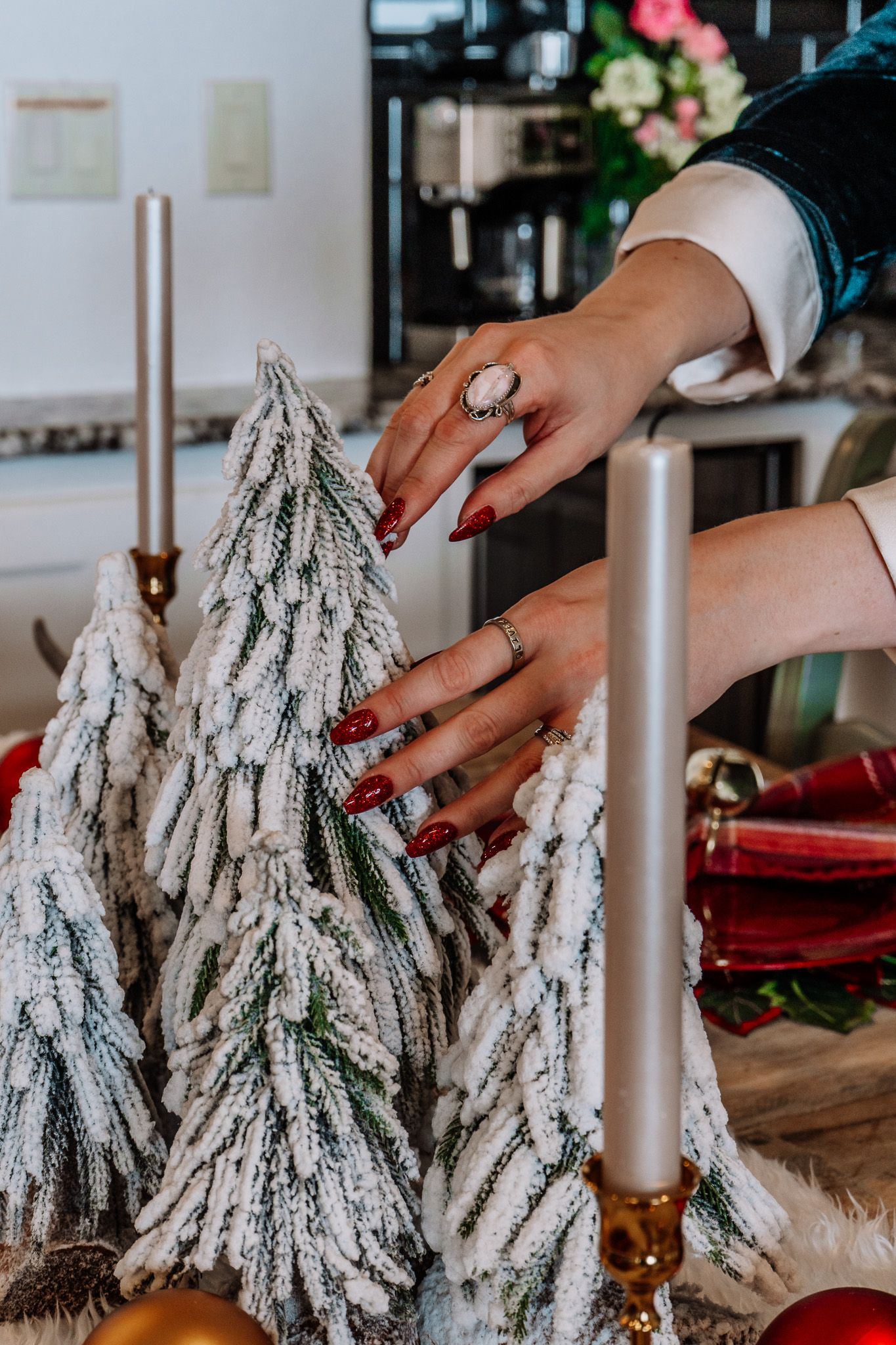 Hands with red nails arranging snowy artificial Christmas trees on a table.