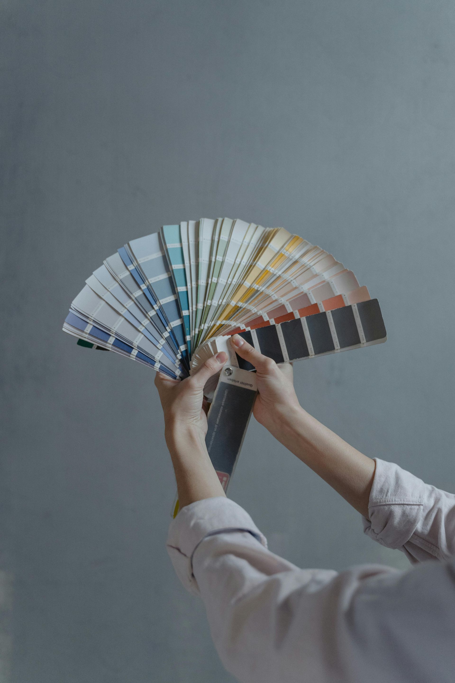 Person holding up a fan of paint color swatches against a gray wall.