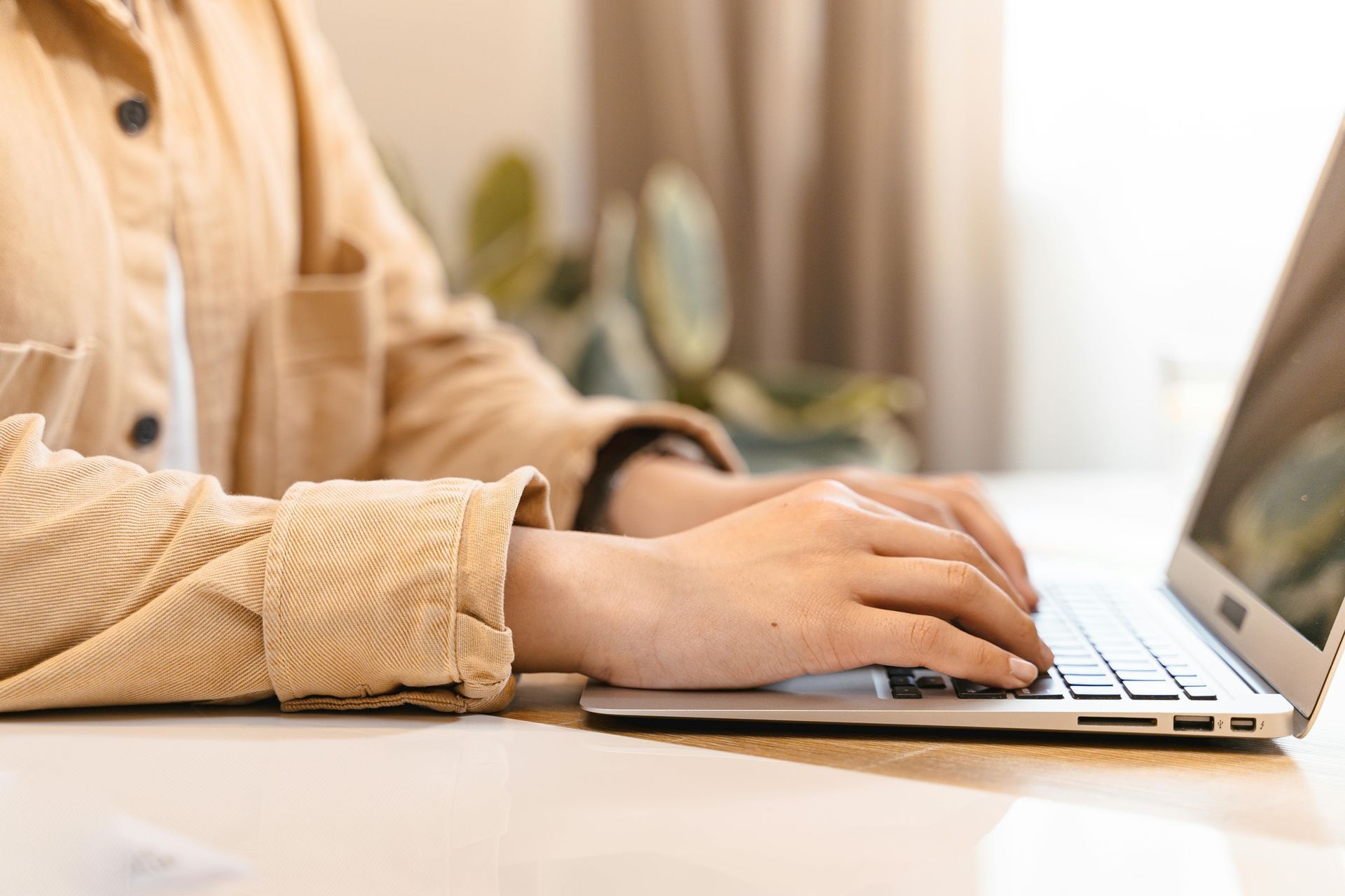 Person typing on laptop, seated at a desk, wearing a tan corduroy shirt.