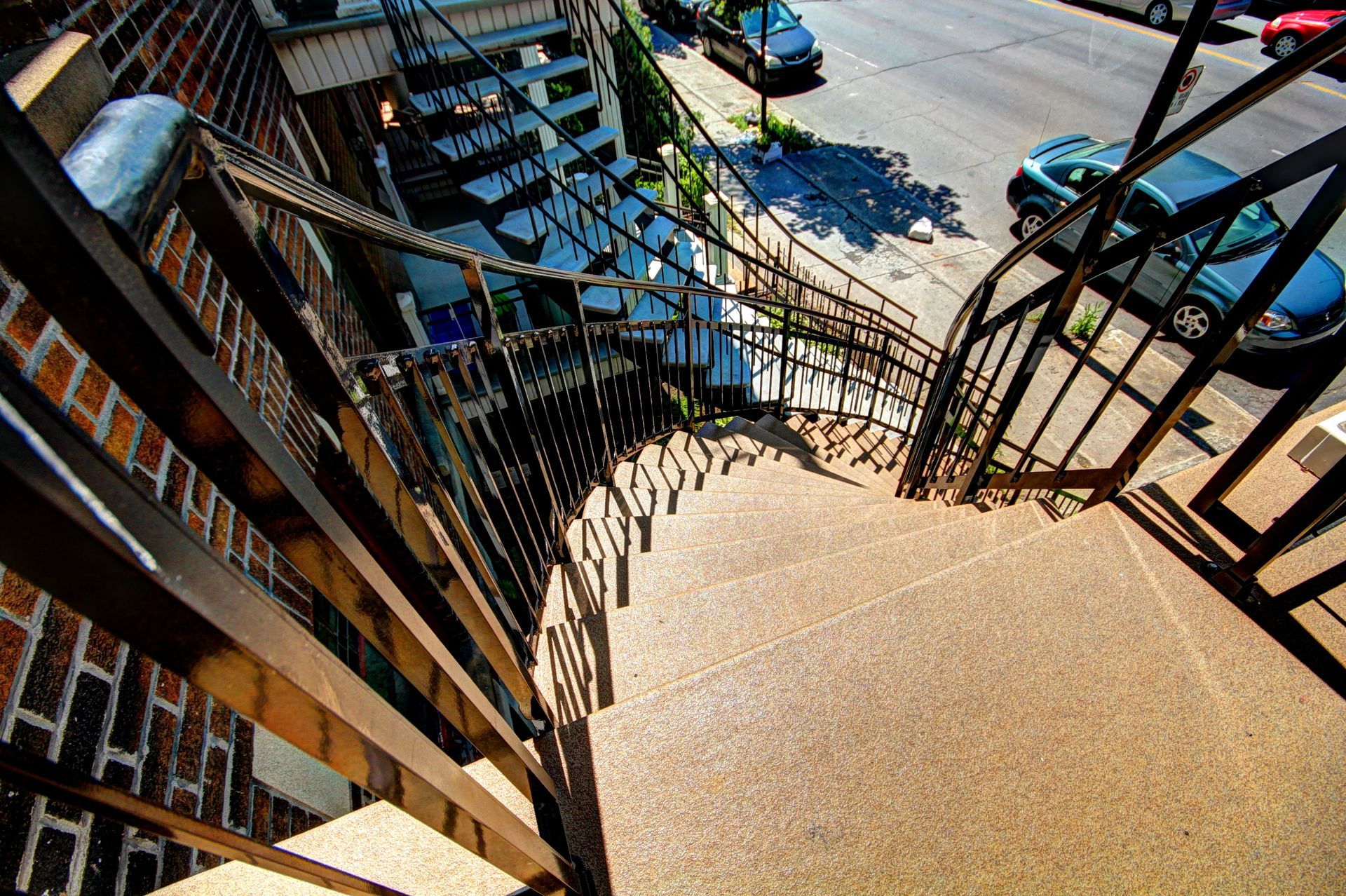 Un escalier menant à un immeuble avec des voitures garées au bord de la route.