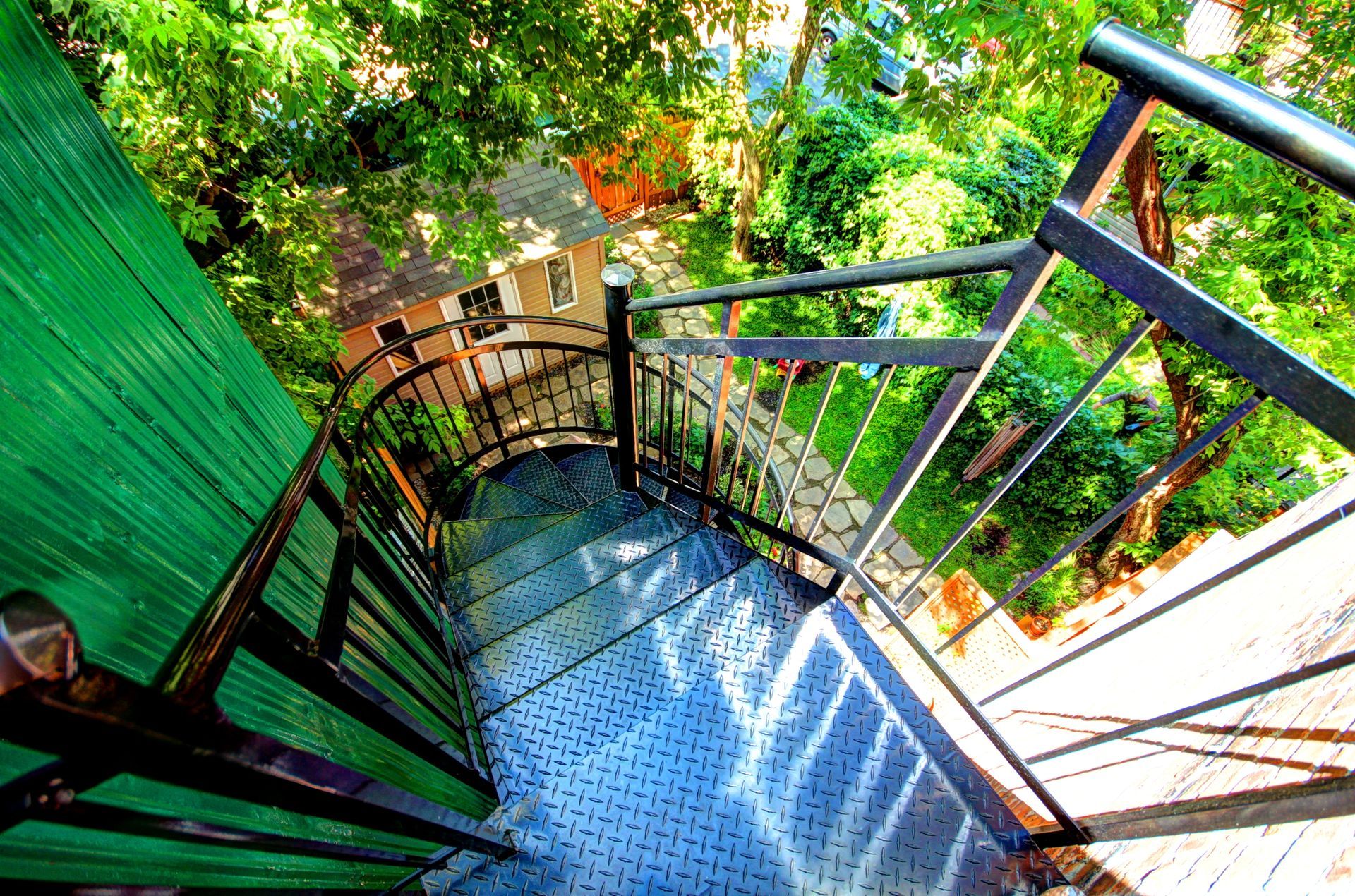 Un escalier en colimaçon menant à un bâtiment vert entouré d'arbres.