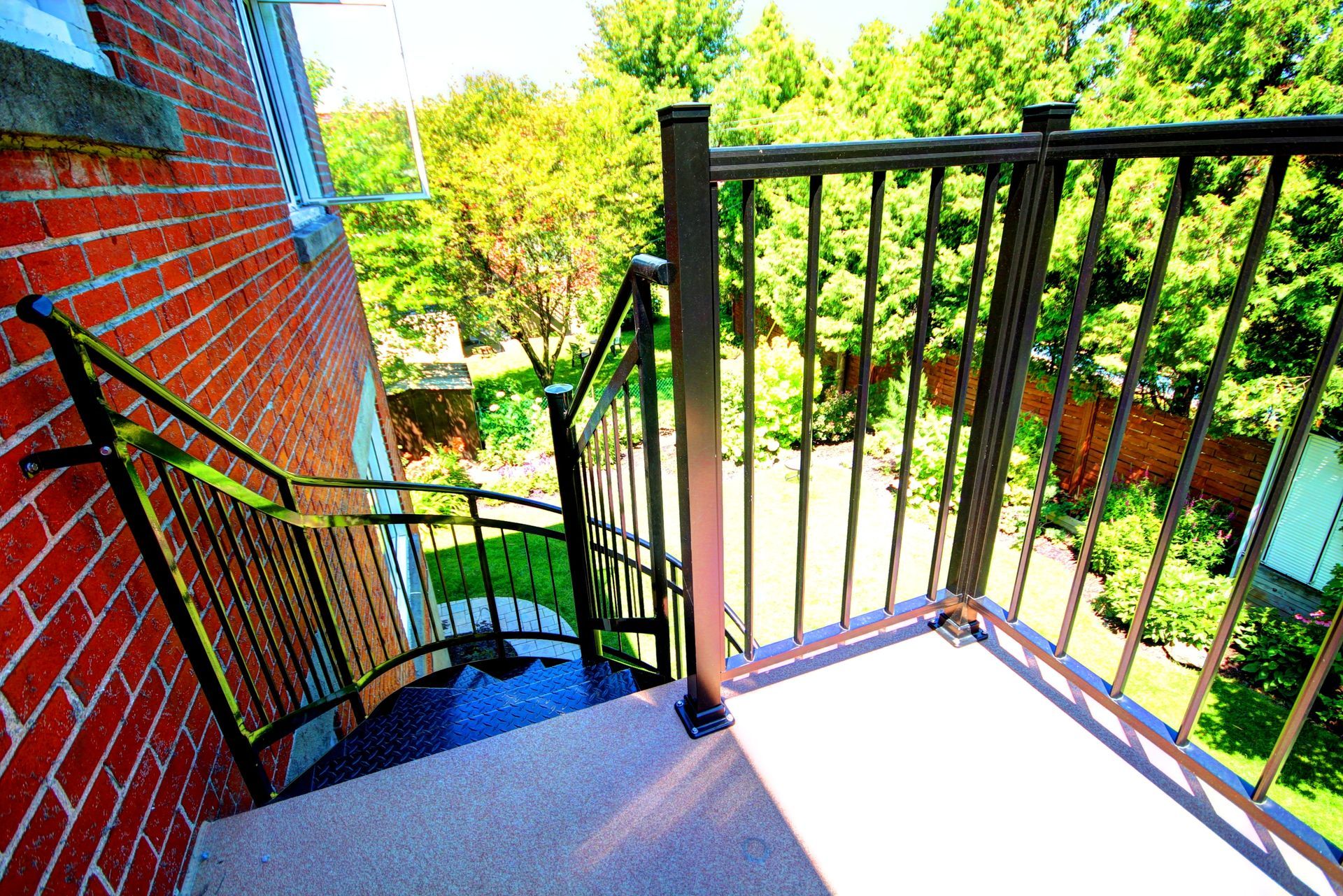 Un escalier en colimaçon avec une rampe métallique menant à un bâtiment en brique