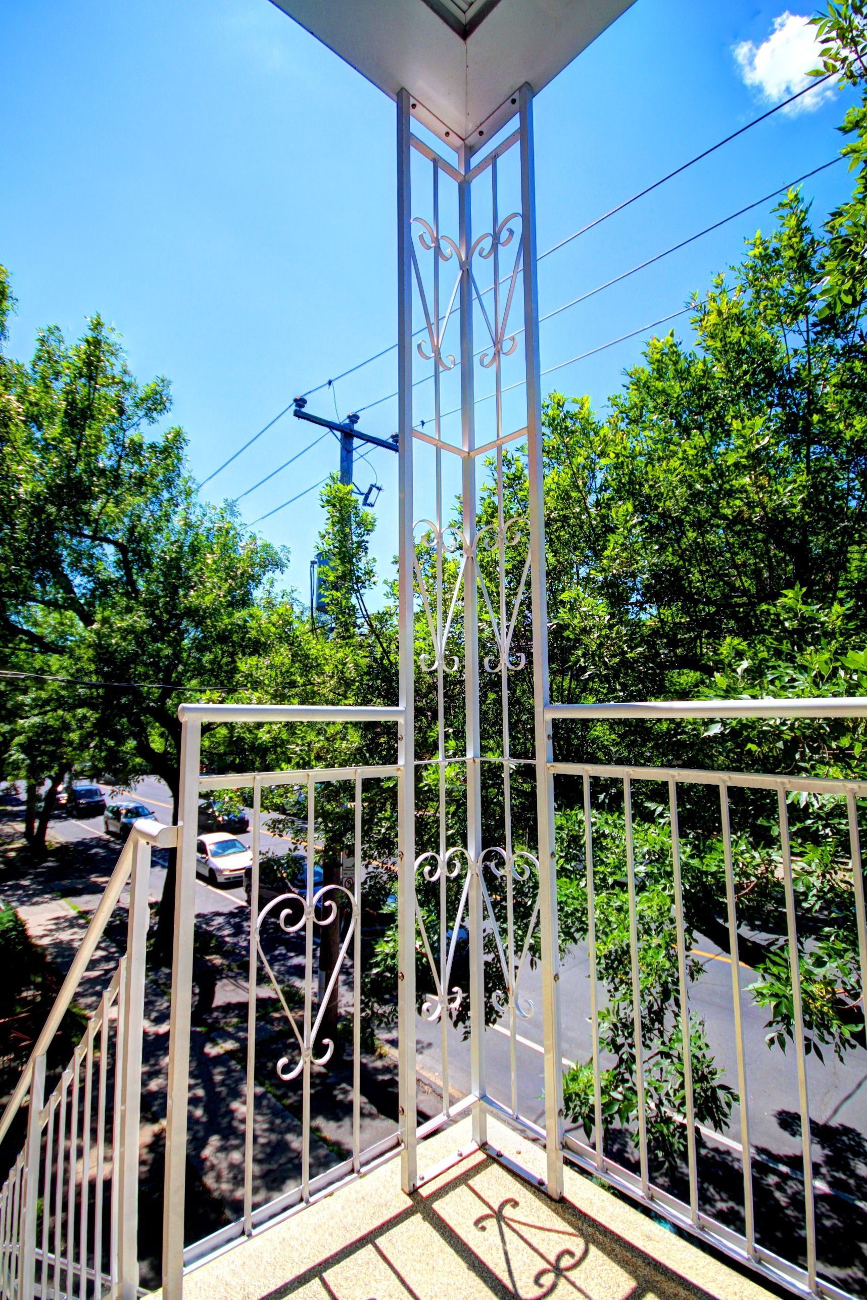 Un balcon avec une balustrade en fer forgé donnant sur une rue et des arbres.