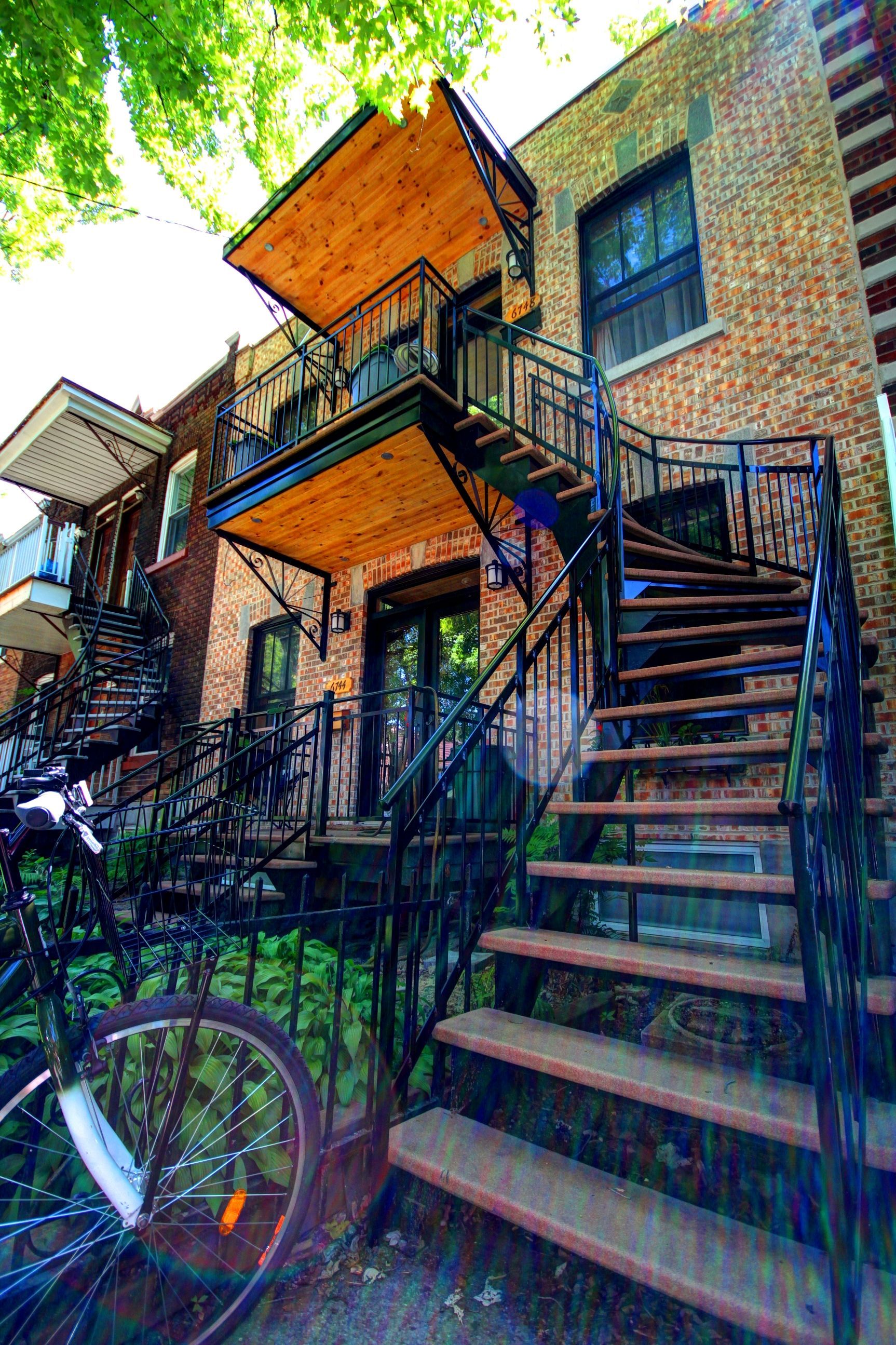 Un vélo est garé devant un immeuble auquel on accède par des escaliers.