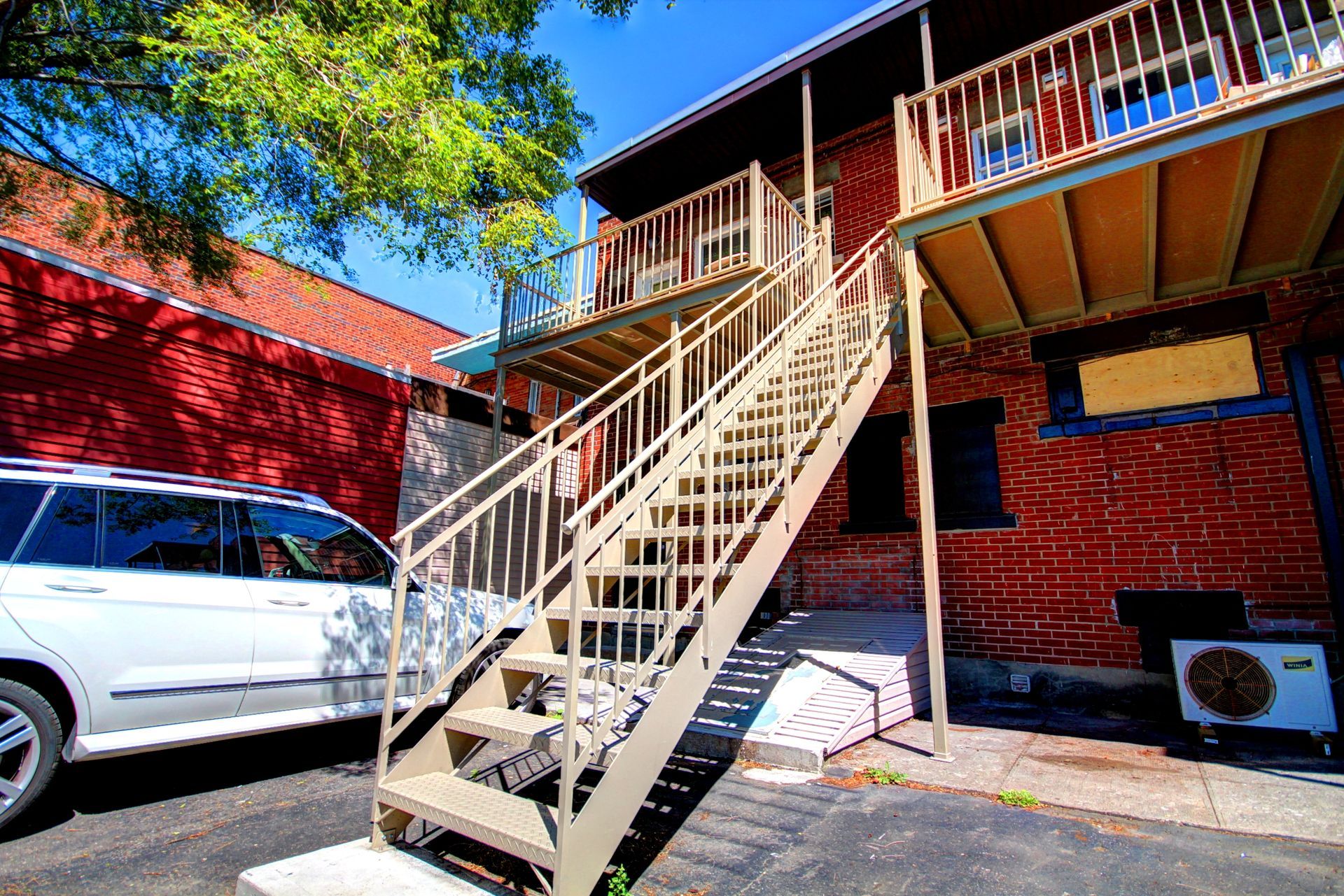 Un SUV blanc est garé devant un immeuble avec des escaliers menant au deuxième étage.
