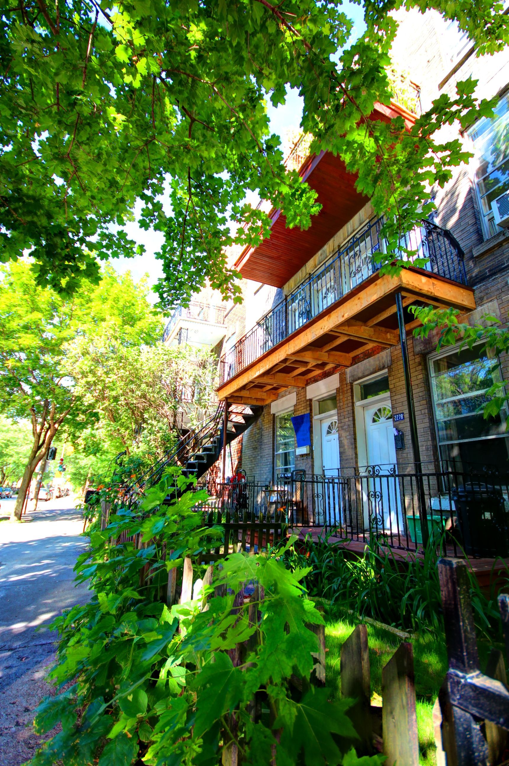 Un immeuble avec balcon et escaliers est entouré d'arbres.