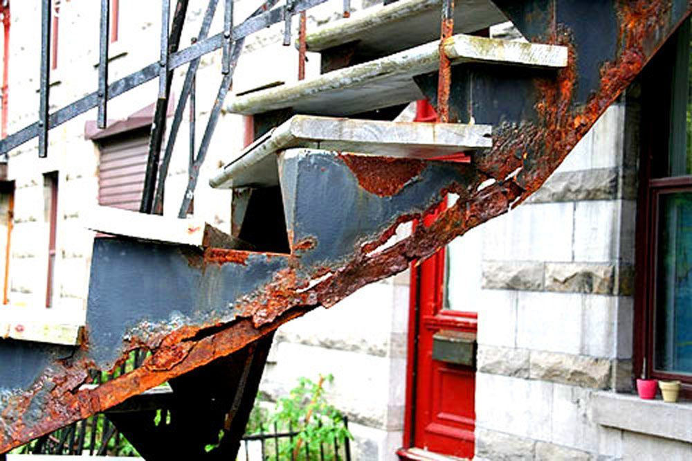 Un escalier rouillé se trouve à l'extérieur d'un bâtiment à côté d'une porte rouge.