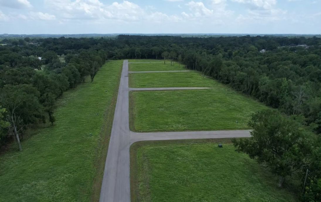 Aerial view of a paved road beside grassy clearing and dense green forest under a cloudy sky