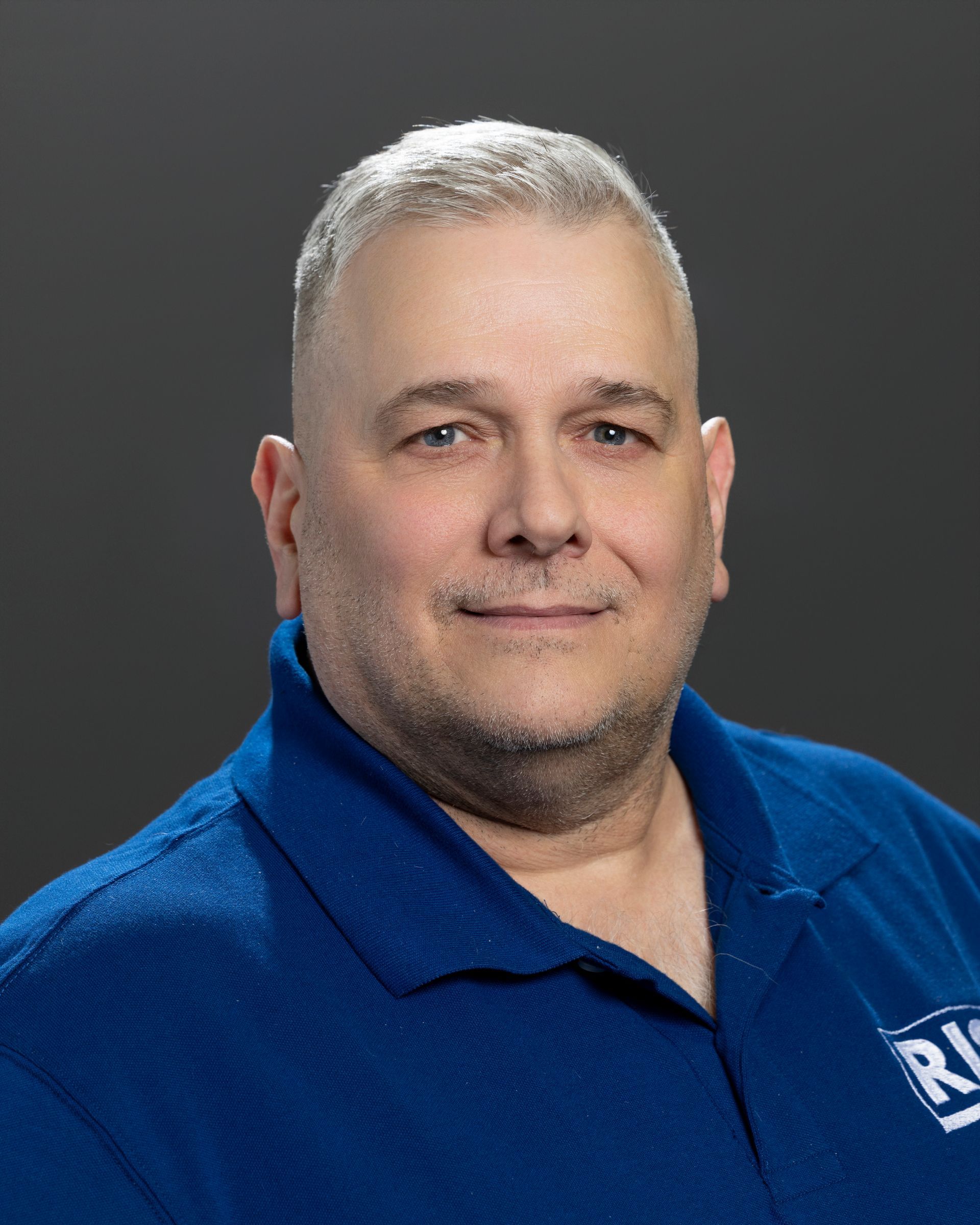 A man in a blue shirt and blue tie is smiling for the camera.