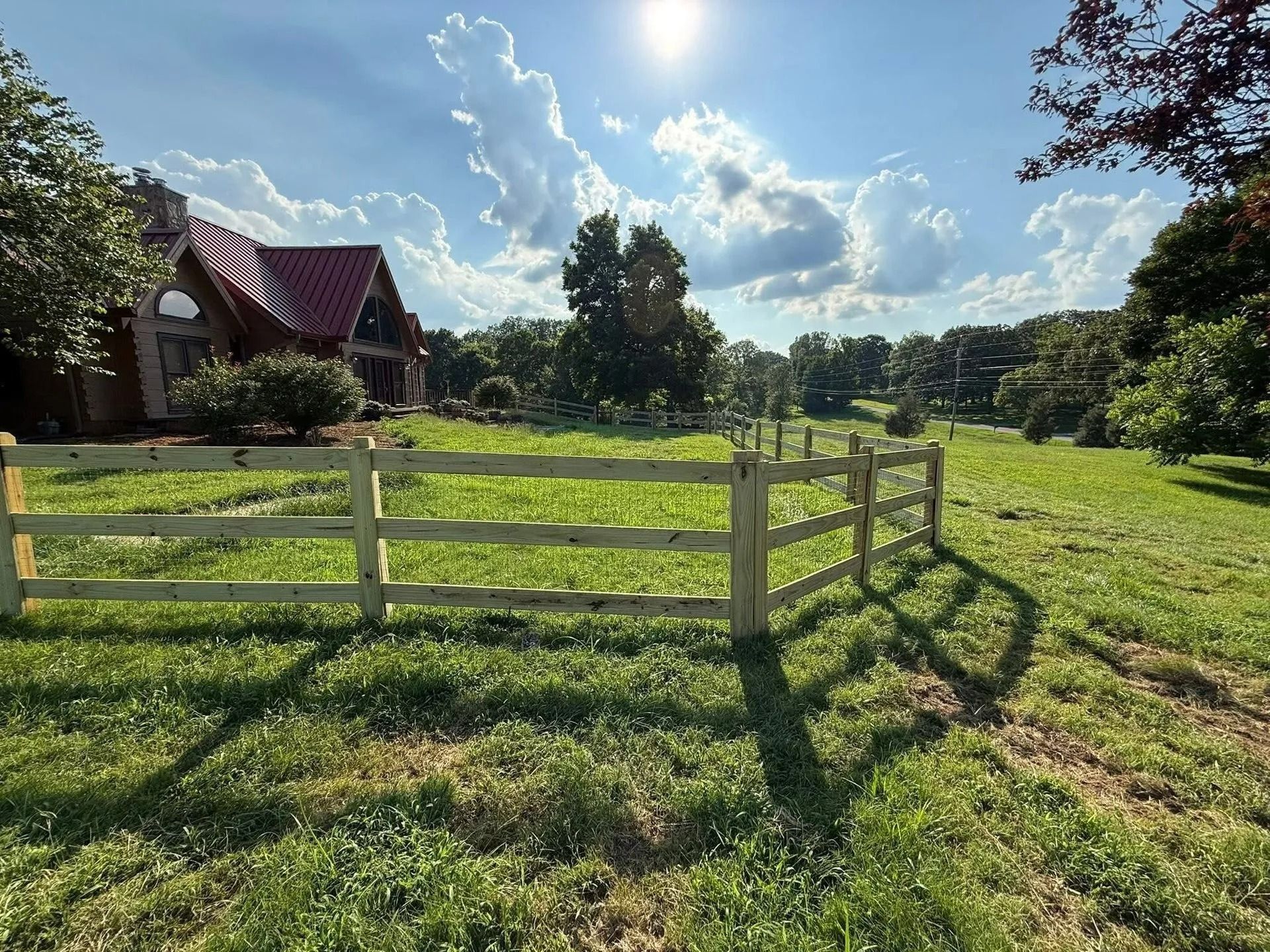 Wooden fence in a grassy field on a sunny day with a house in the background.