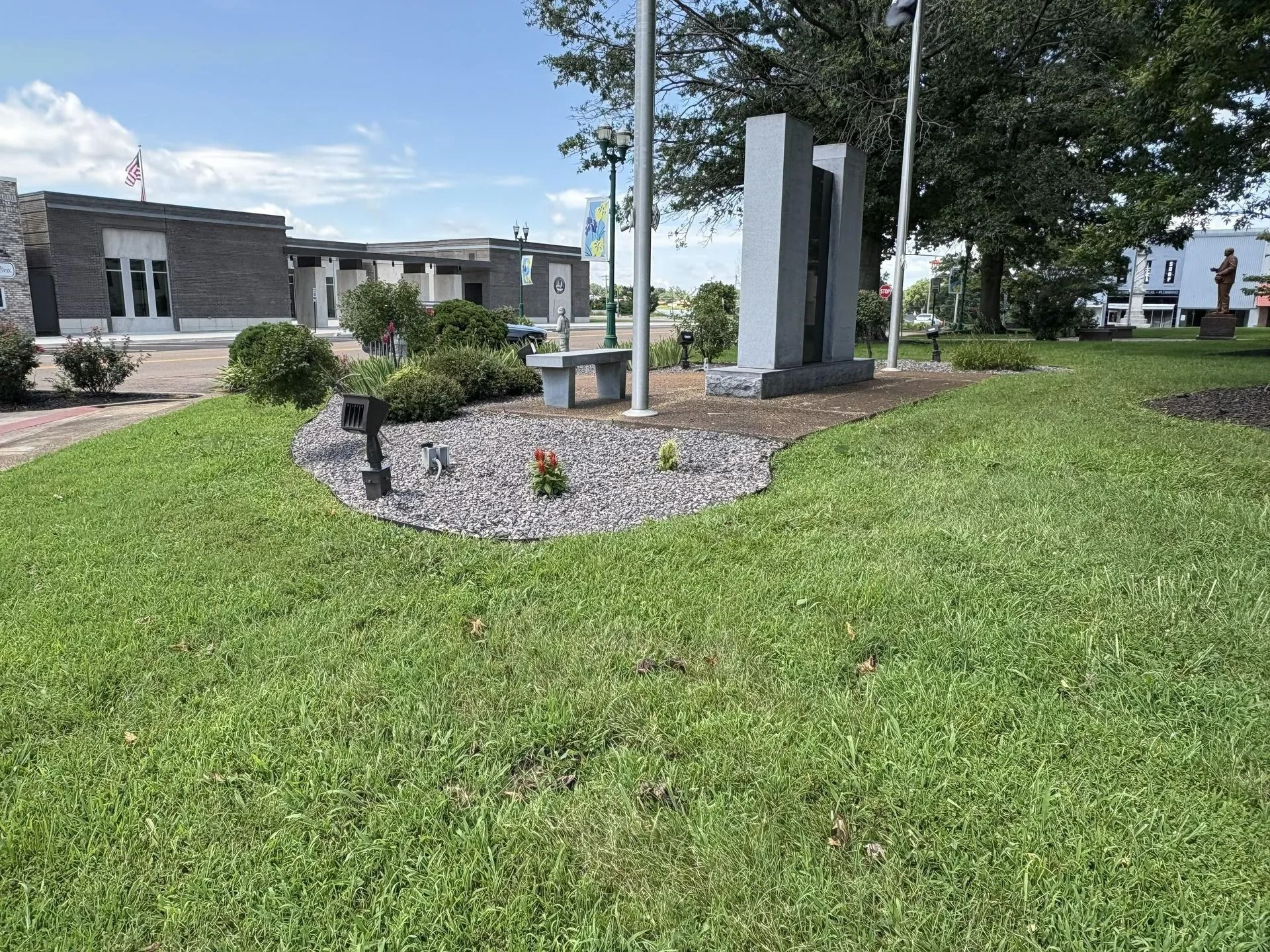Exterior view of a park with a grey sculpture and a building in the background on a sunny day.