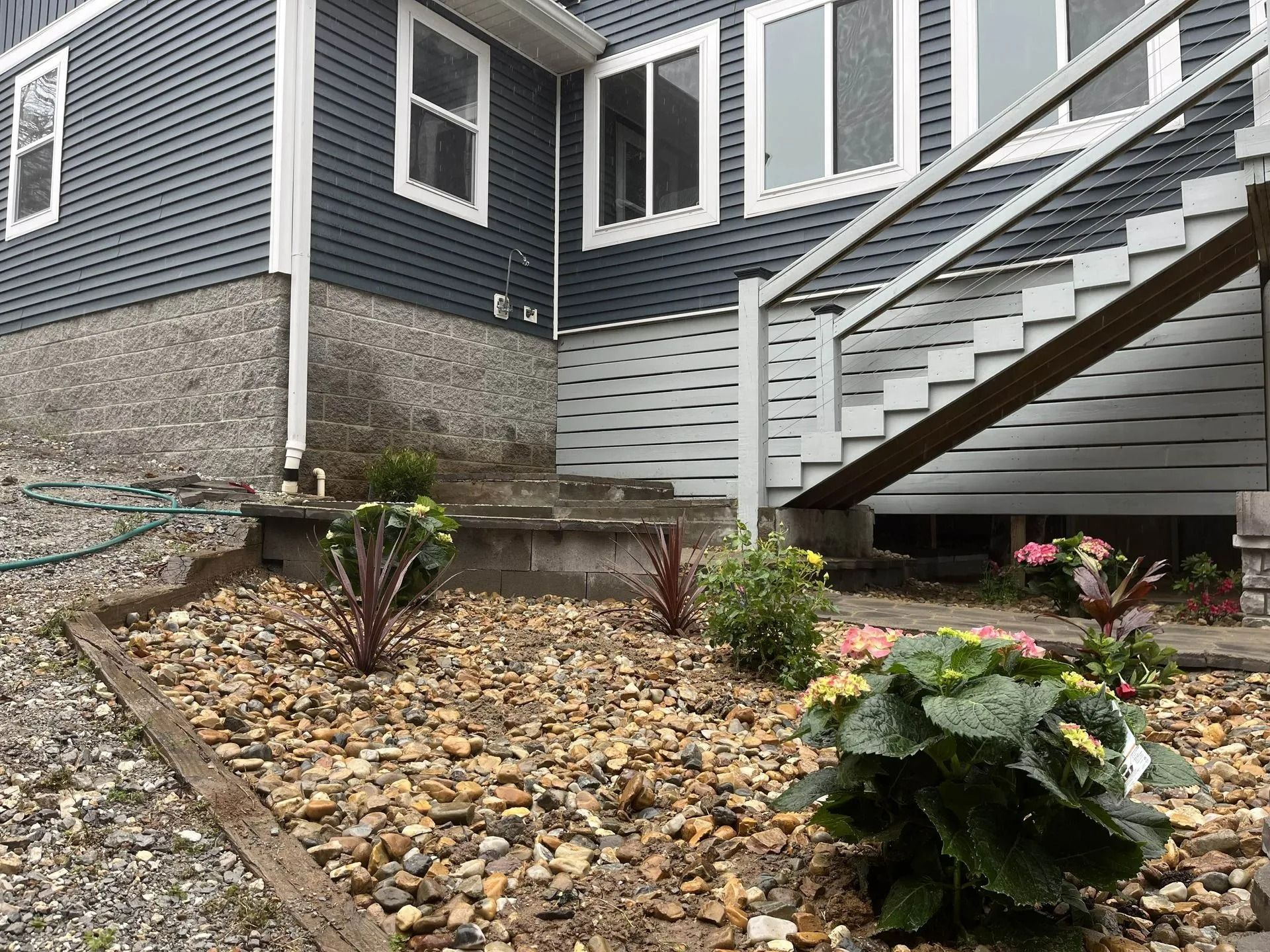 A house with blue siding and stairs, next to a garden bed filled with rocks and plants.