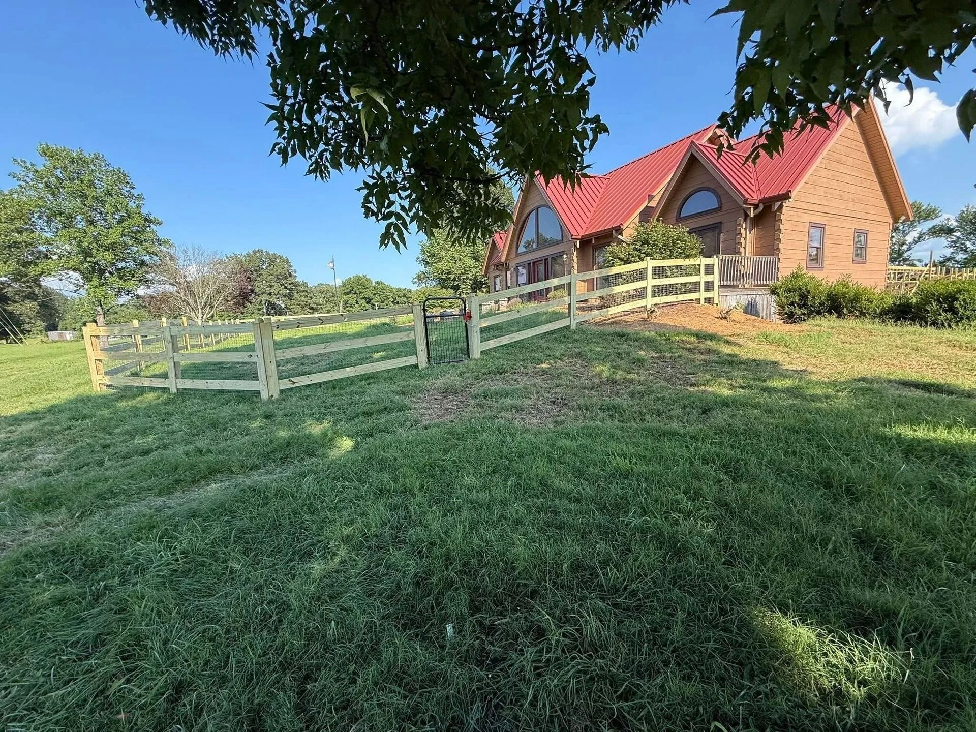 House with red roof, wooden fence, and green grass on a sunny day.