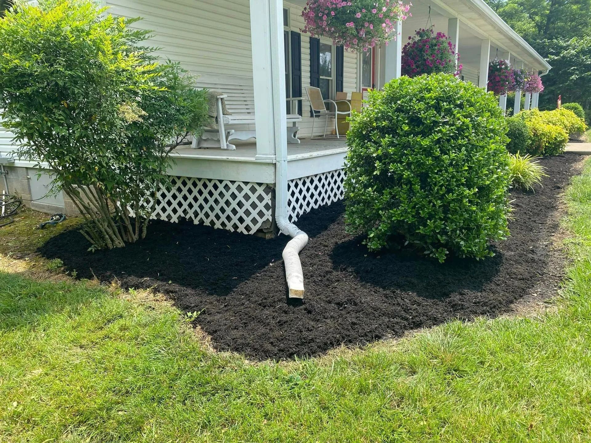 House with white porch, flower beds with black mulch, and green lawn.
