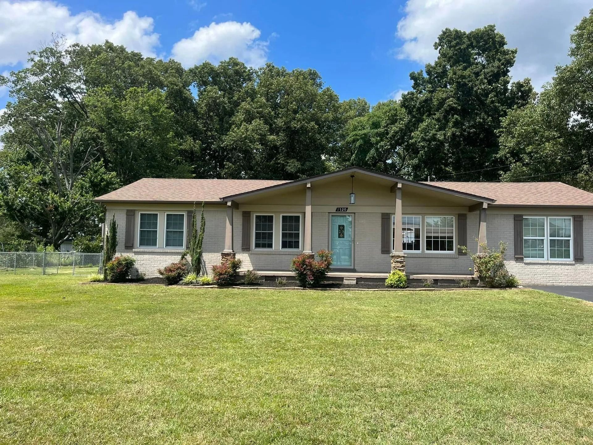 Ranch-style house with blue door and beige siding, set on a green lawn with trees in the background.