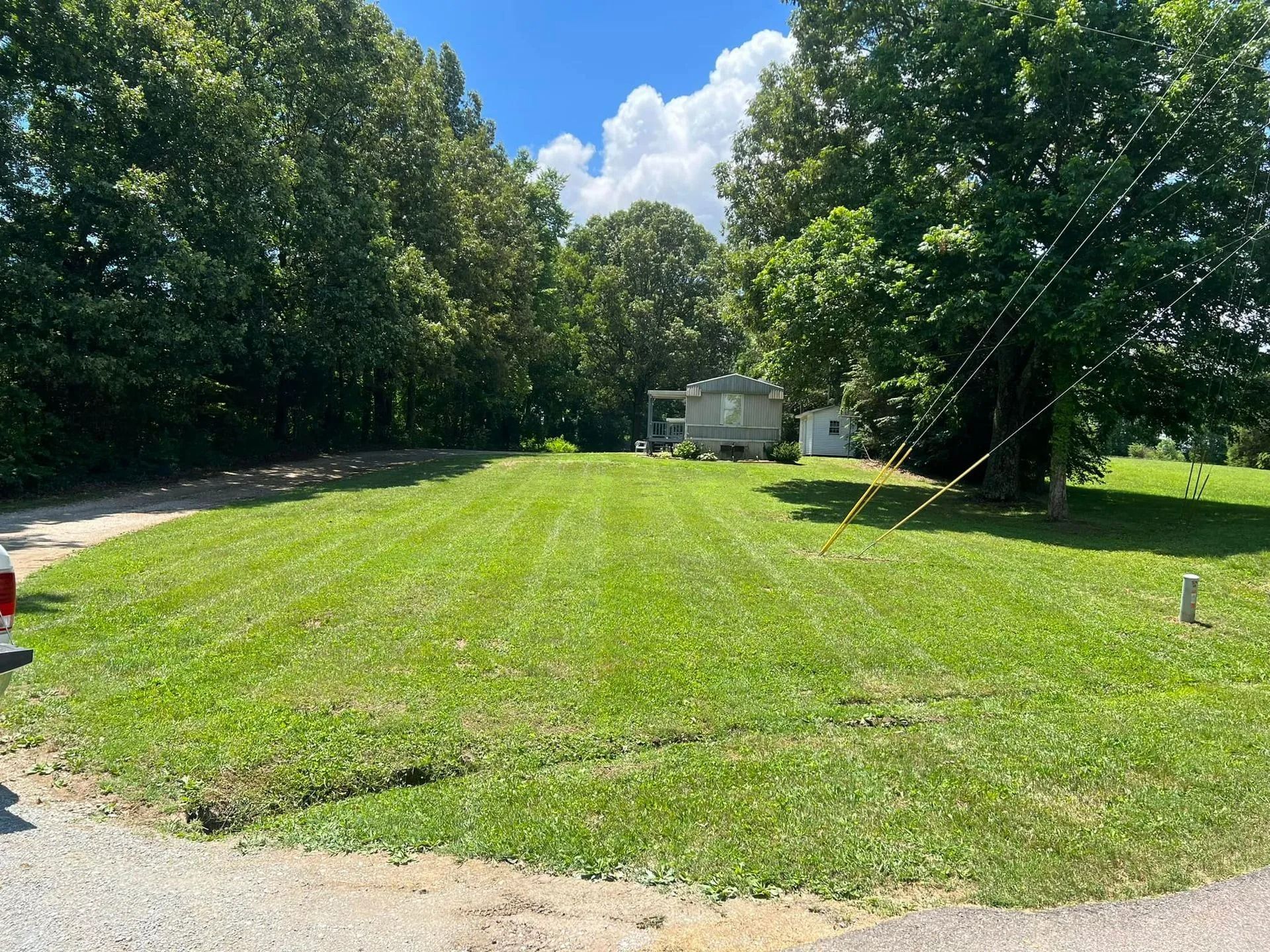 Lawn in front of a small building and trees. Sky visible. Green grass, paved road.