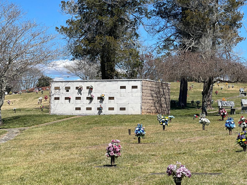 A cemetery filled with lots of flowers and a white building.