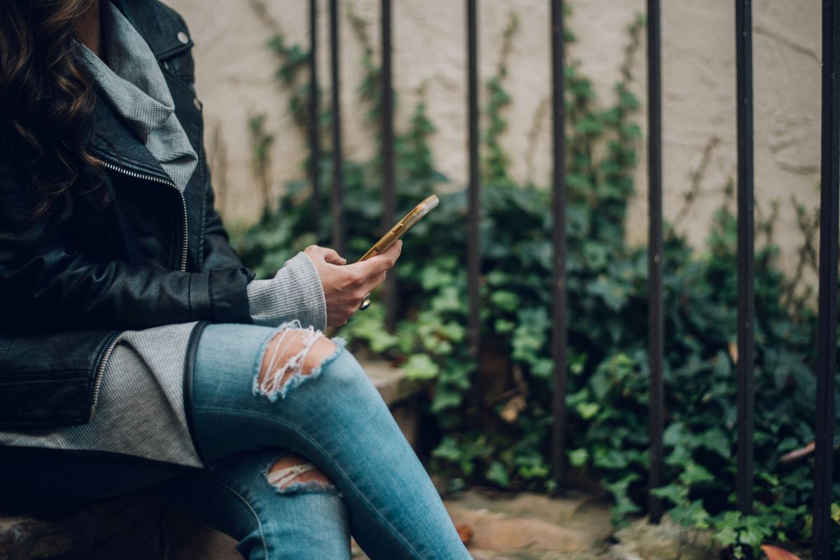 A woman is sitting on a ledge looking at her cell phone.