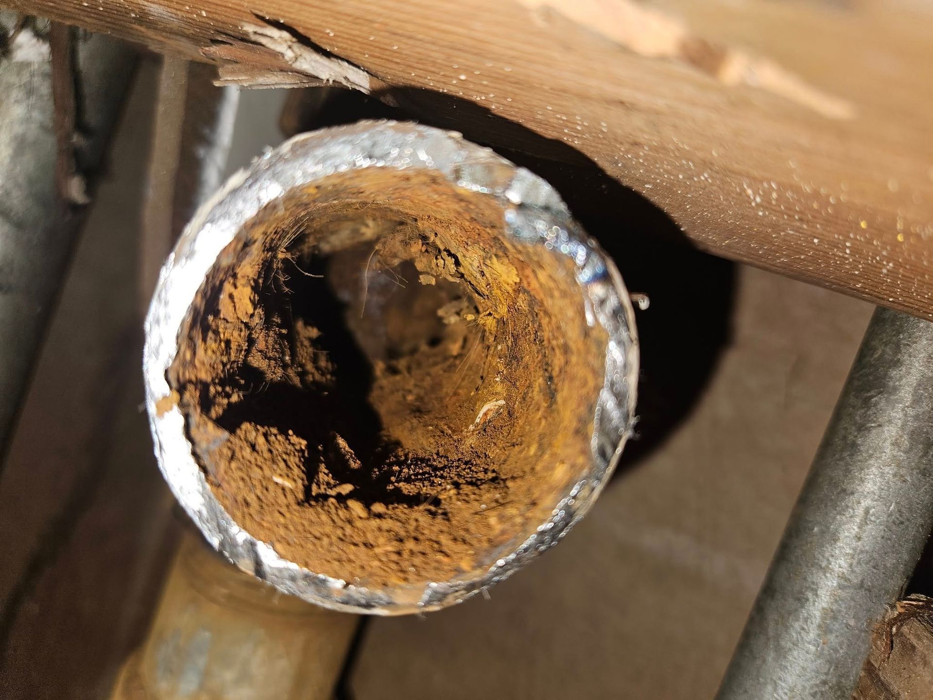 Corroded water pipe opening, brown rust buildup inside. Silver wrap around the pipe, seen from above.