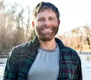 Man in green plaid shirt smiling outdoors.