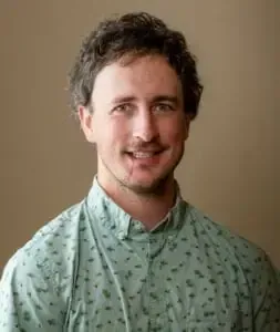 Man with curly brown hair, wearing a teal patterned button-down shirt, smiling.