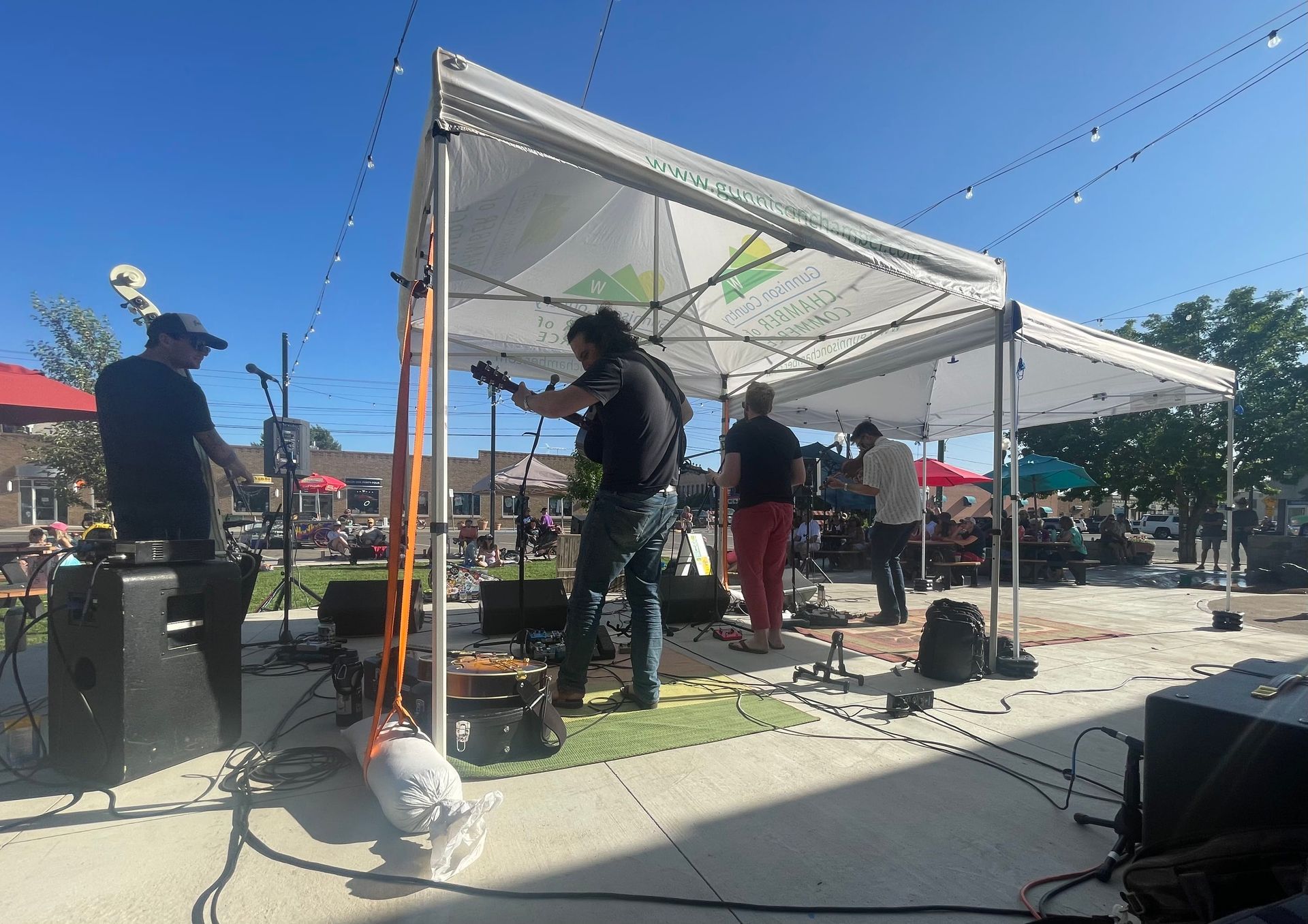 Band playing under a white canopy on a sunny day in an outdoor square.