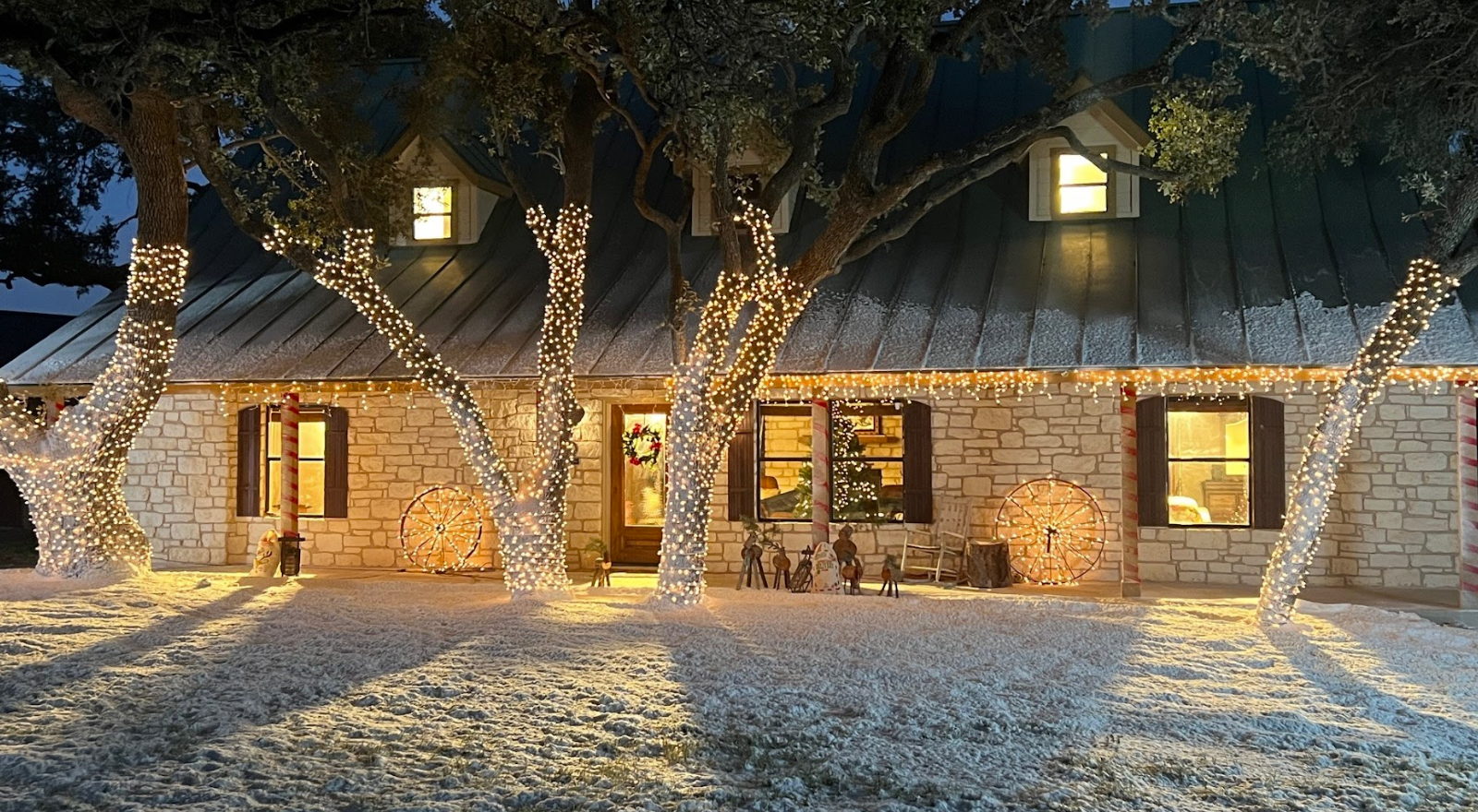 Stone ranch house with illuminated trees and snow-covered yard
