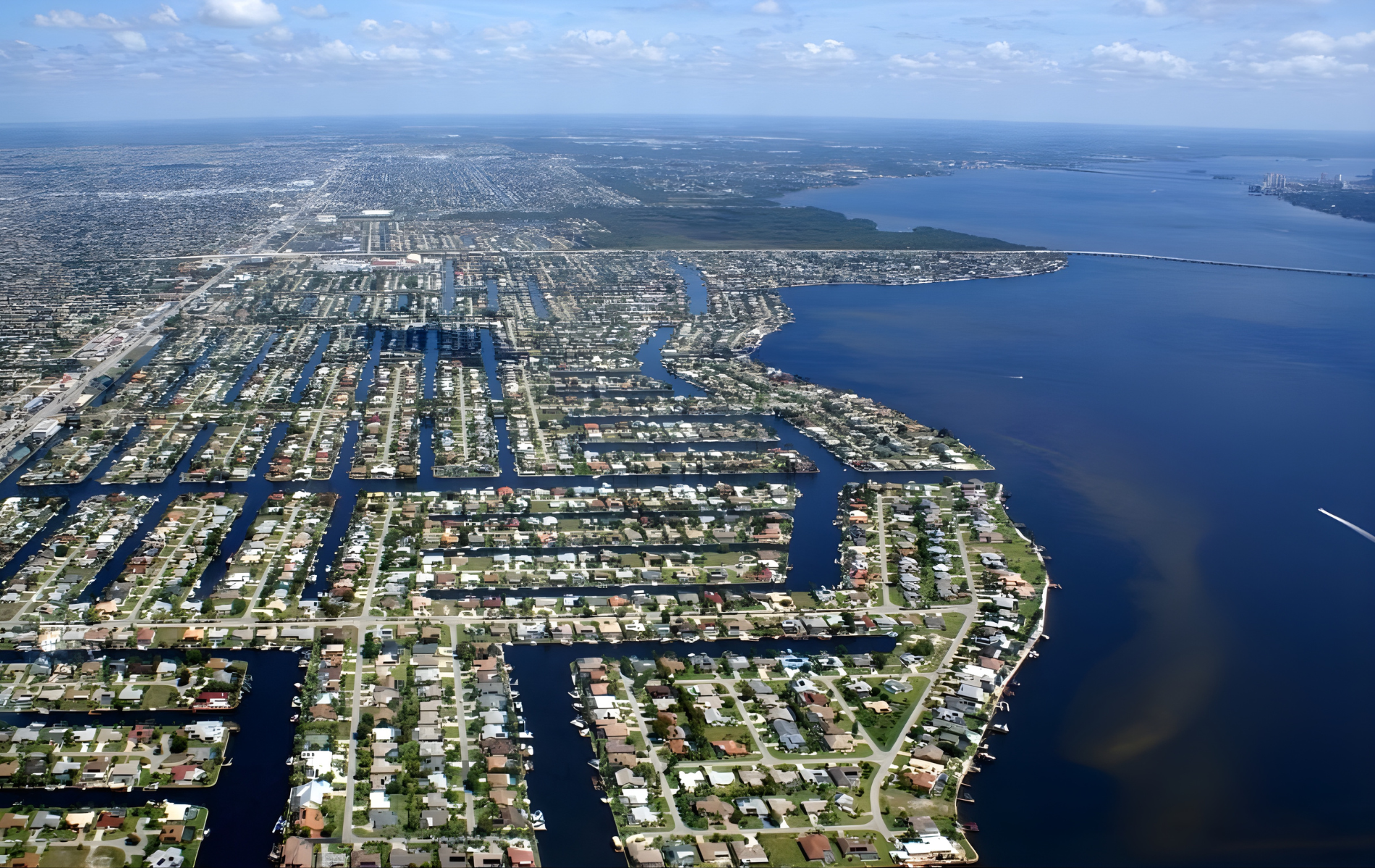 Aerial view of a coastal city with a network of canals and houses, bordered by water and a bridge.