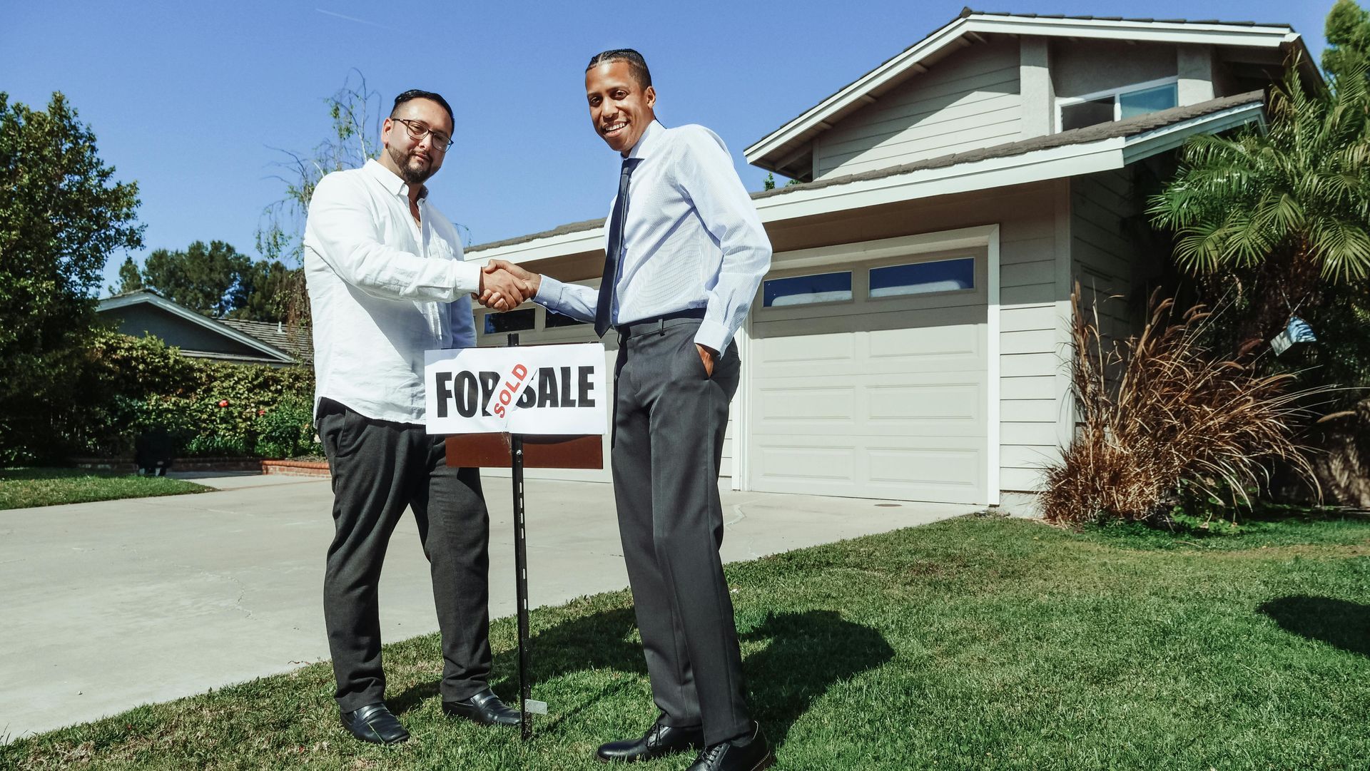 Two men shaking hands in front of a house with a 