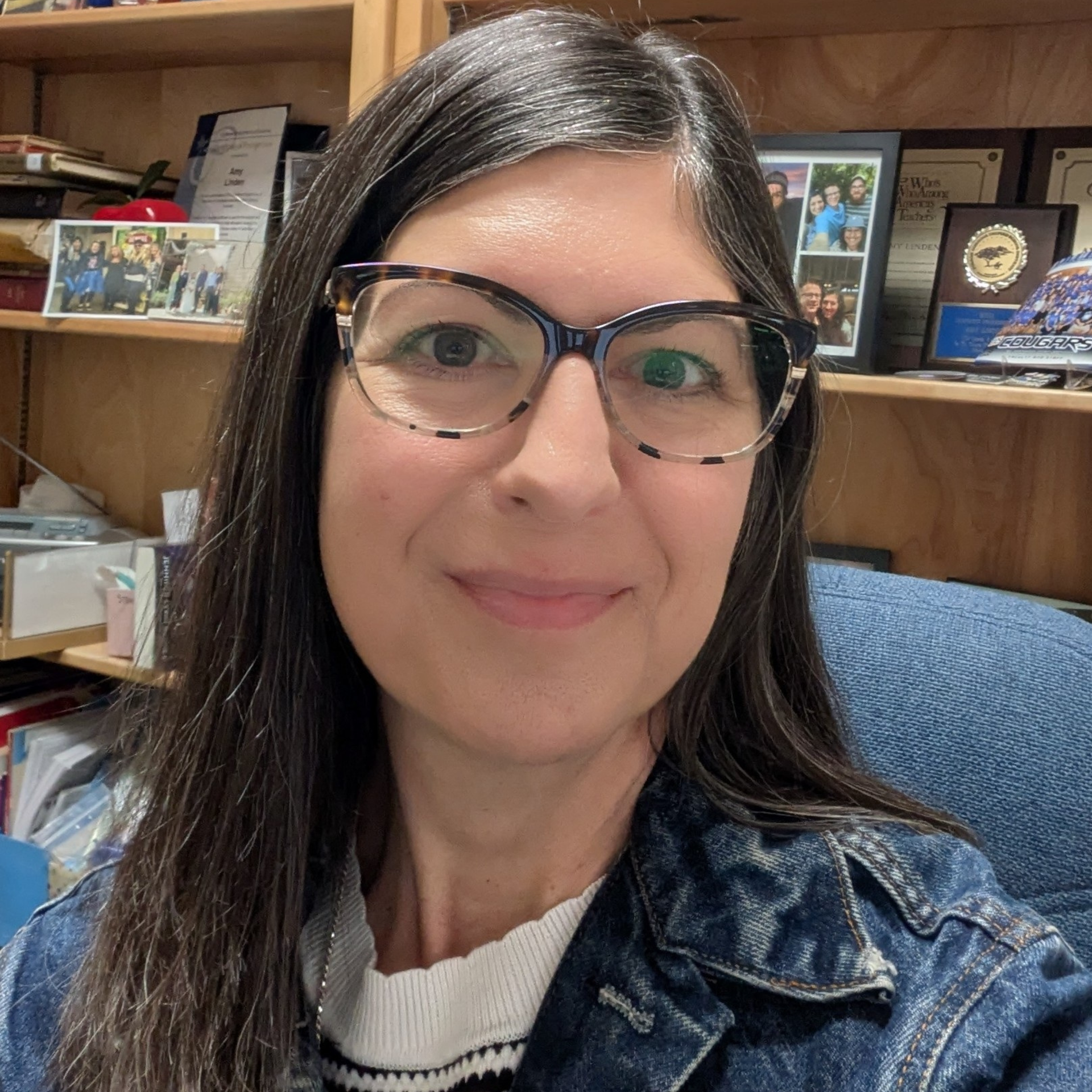 Woman with glasses smiles in front of a bookcase.