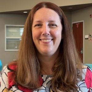 headshot of Kate Applebee with patterned shirt and grey background