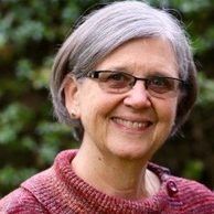 headshot of Katie Williams in red sweater with foliage in background