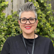 photo of Aimee Korynta wearing black shirt and standing in front of an ivy covered fence