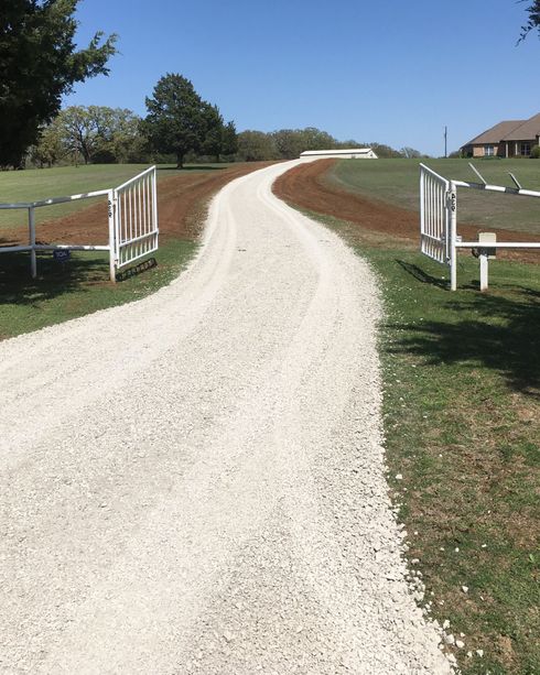 An open white gate on a freshly installed caliche road base on a farm. 