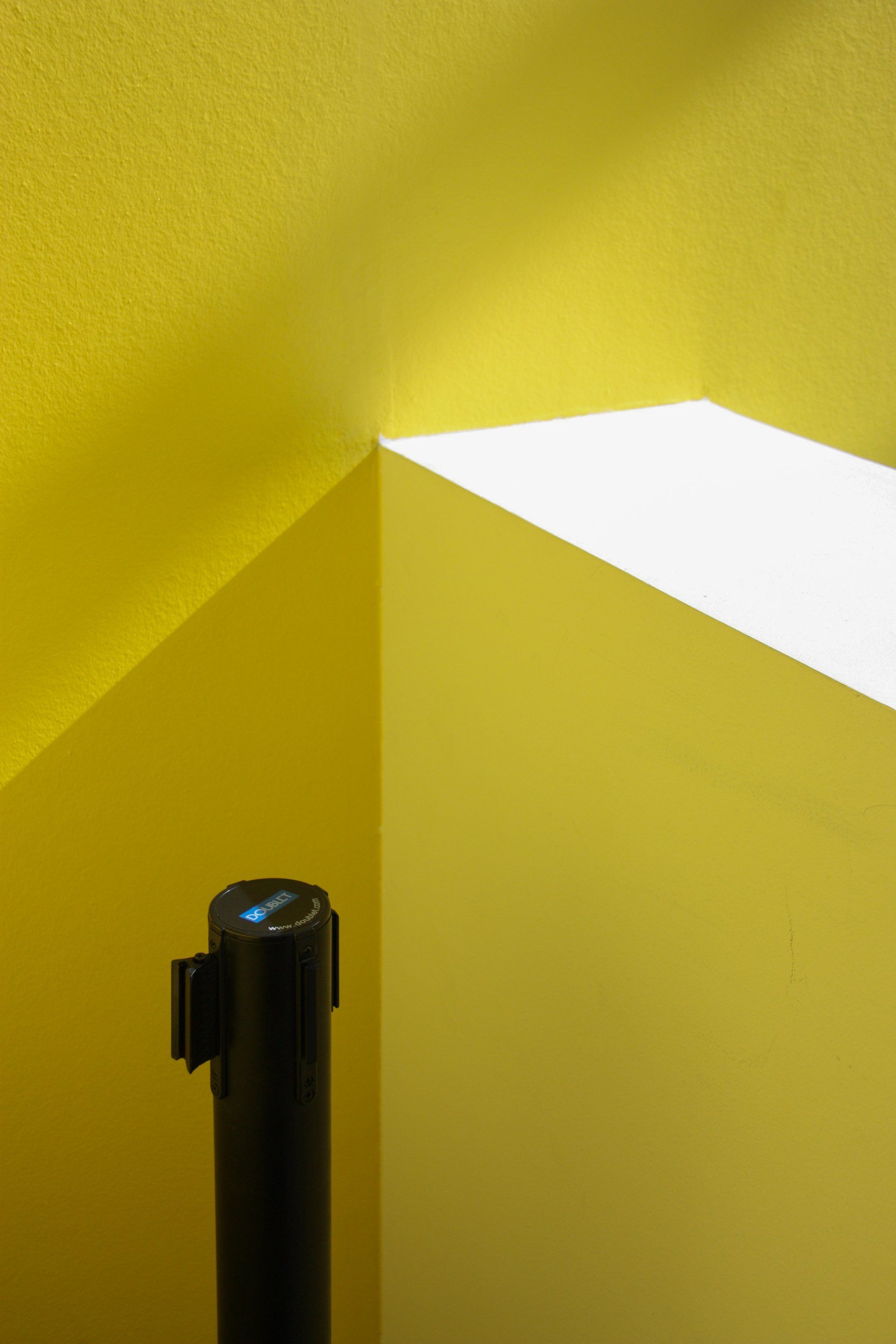 Una paret groga amb un pal negre a la cantonada.