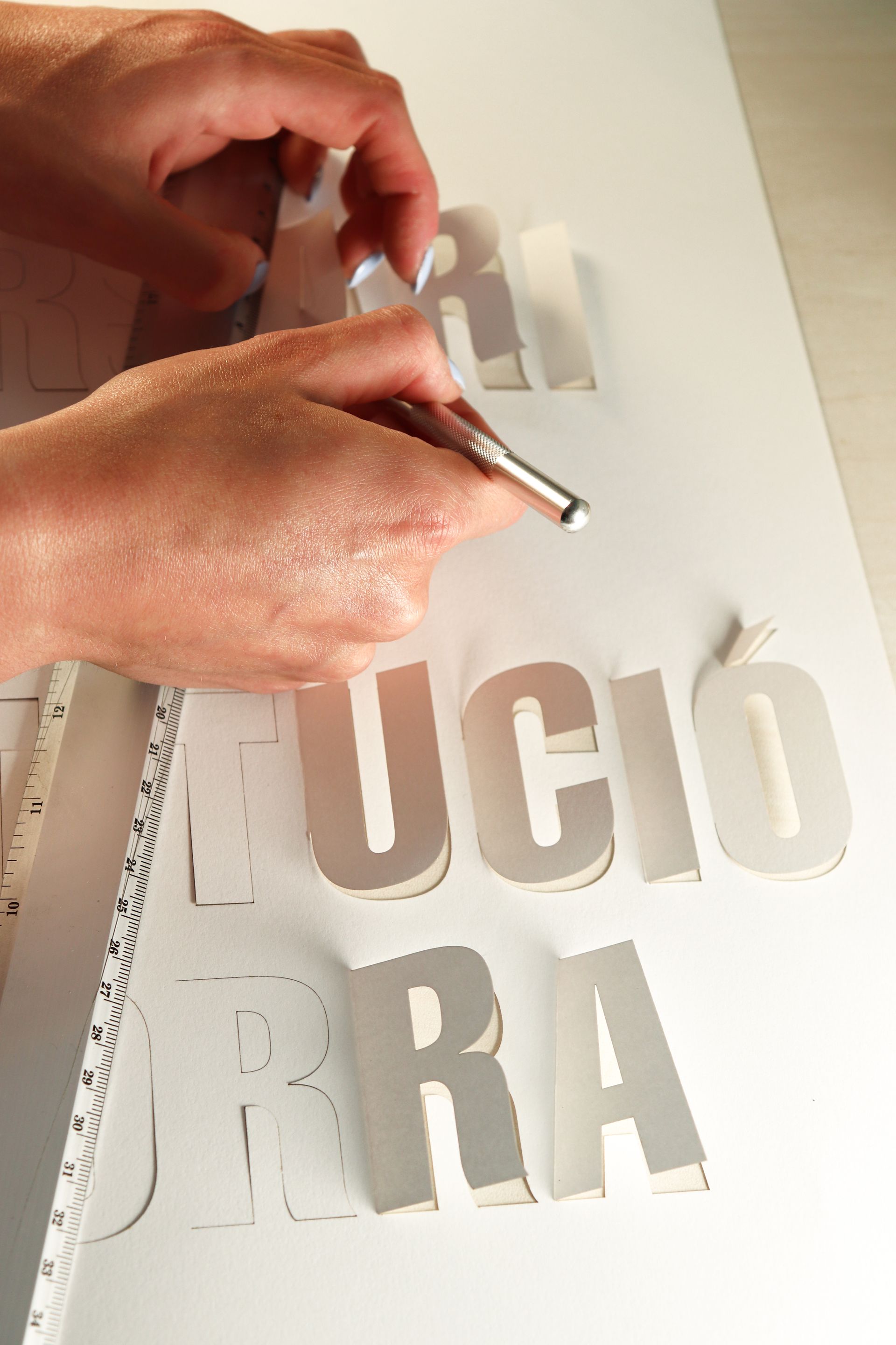 Una persona esta utilizando una regla para cortar con un bisturi unas letras para el cartel comemorativo de la constitución de Andorra. Cartel hecho por Mersi Studio. 